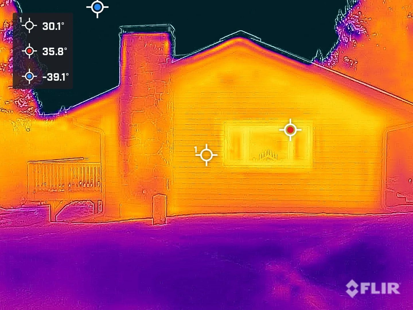 Infrared thermal image of a house at night showing warmer areas in yellow and orange, cooler areas in purple. The house has a chimney, windows, and a fenced yard.