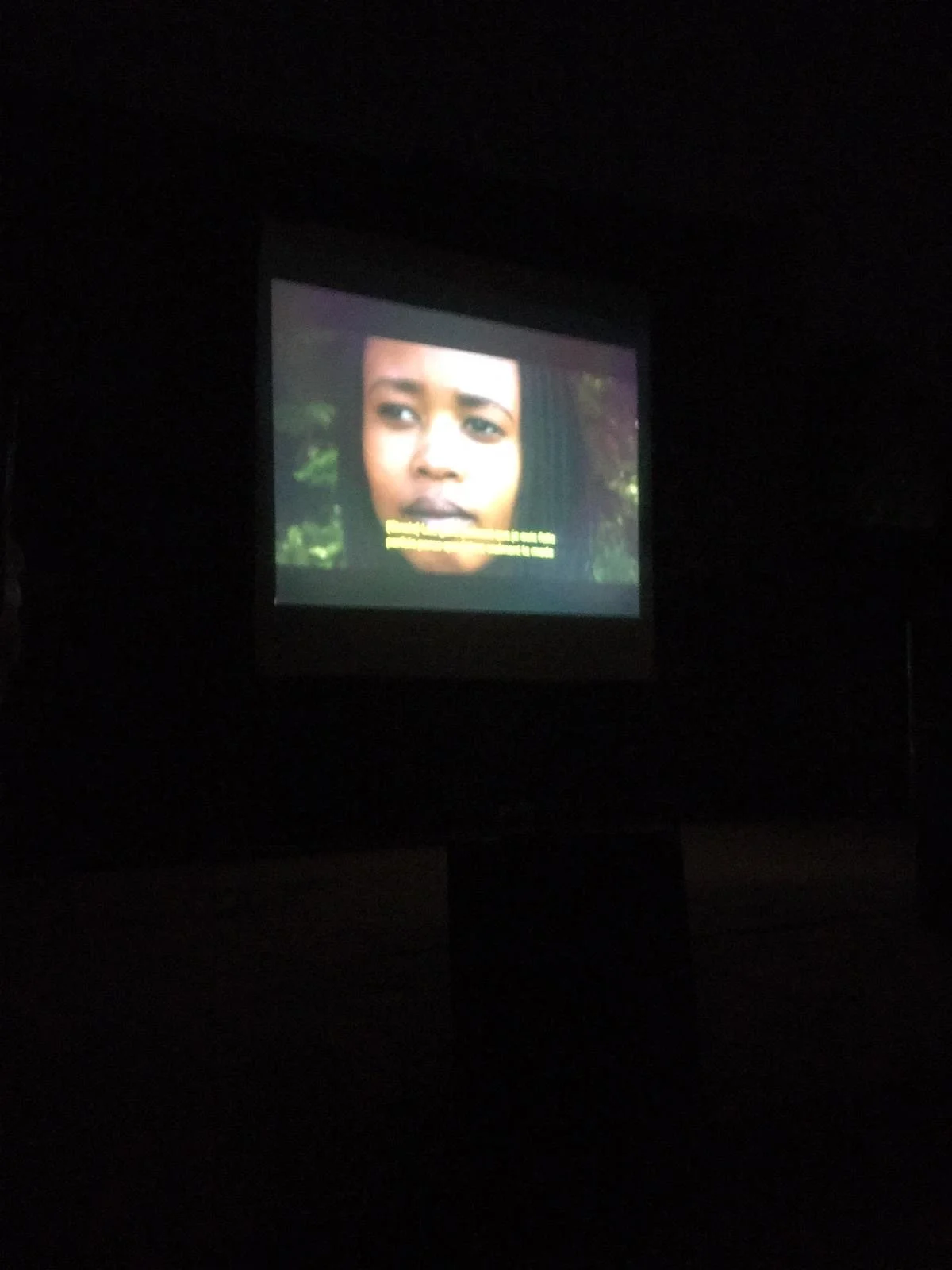 Un écran de projection affichant un visage d'une femme noire avec des sous-titres en français, dans une pièce sombre.