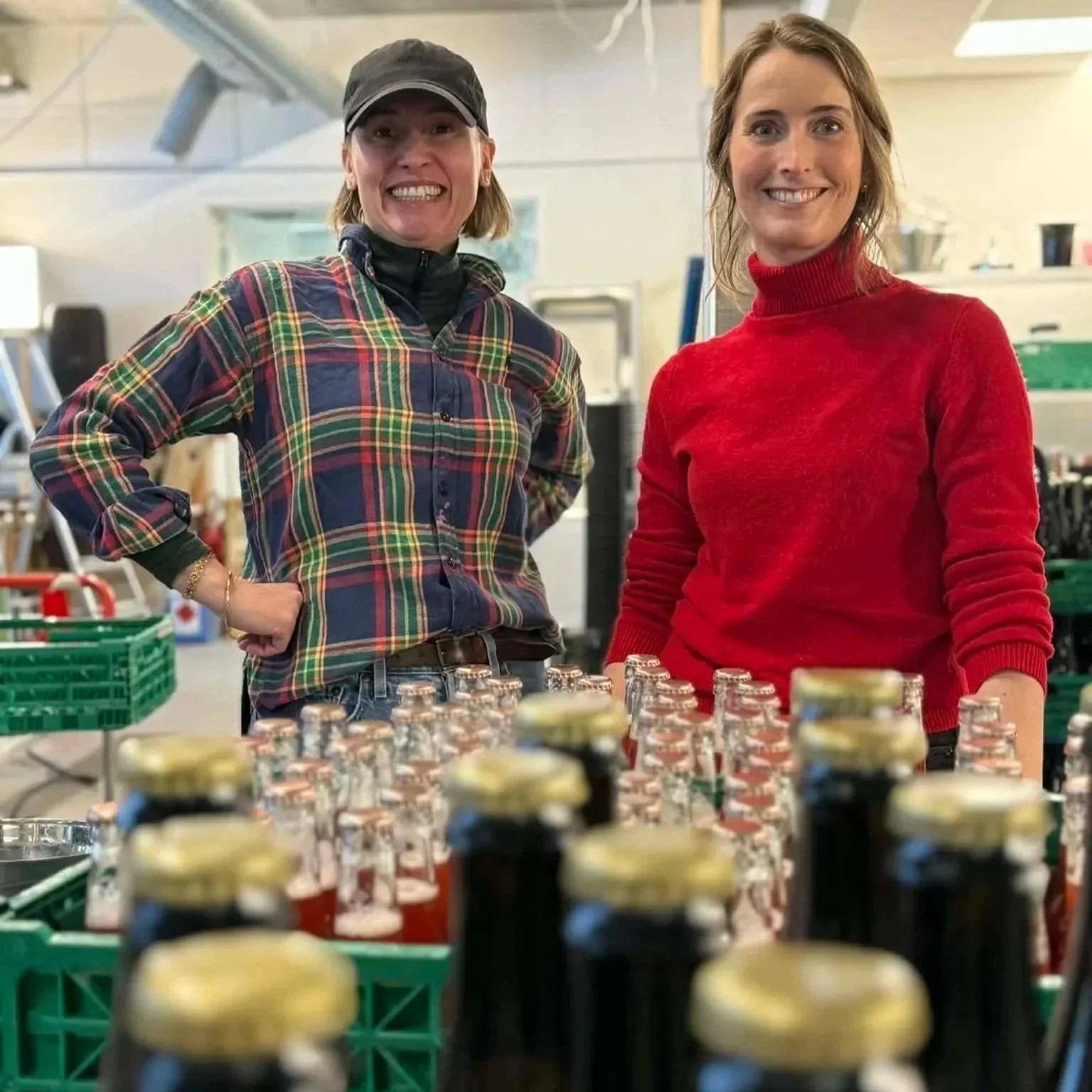 Two women standing behind a table filled with bottled beverages in a store or warehouse, smiling at the camera.