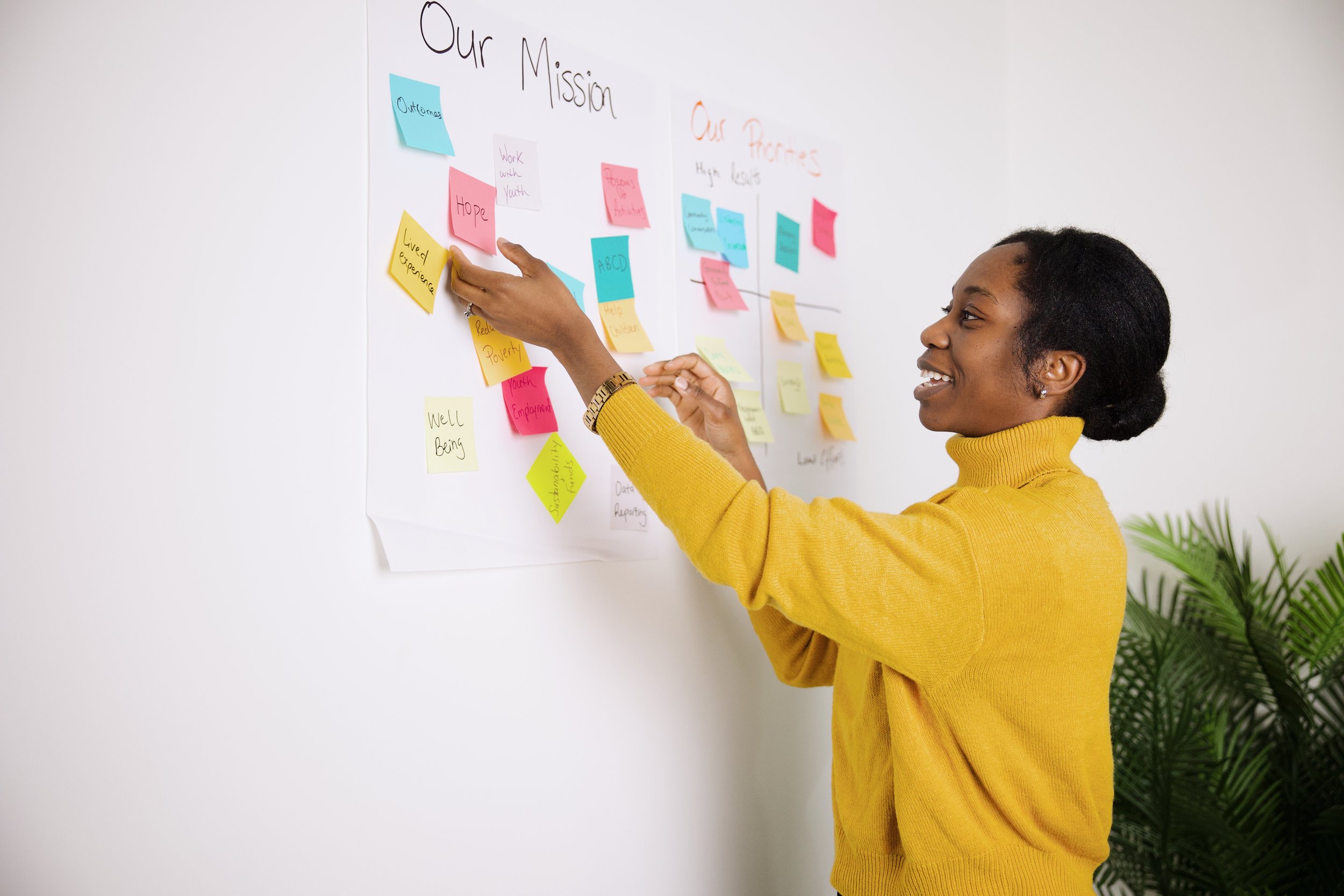 A woman in a yellow sweater sticking colorful sticky notes on a whiteboard titled 'Our Mission' and 'Our Partners' during a discussion or presentation.