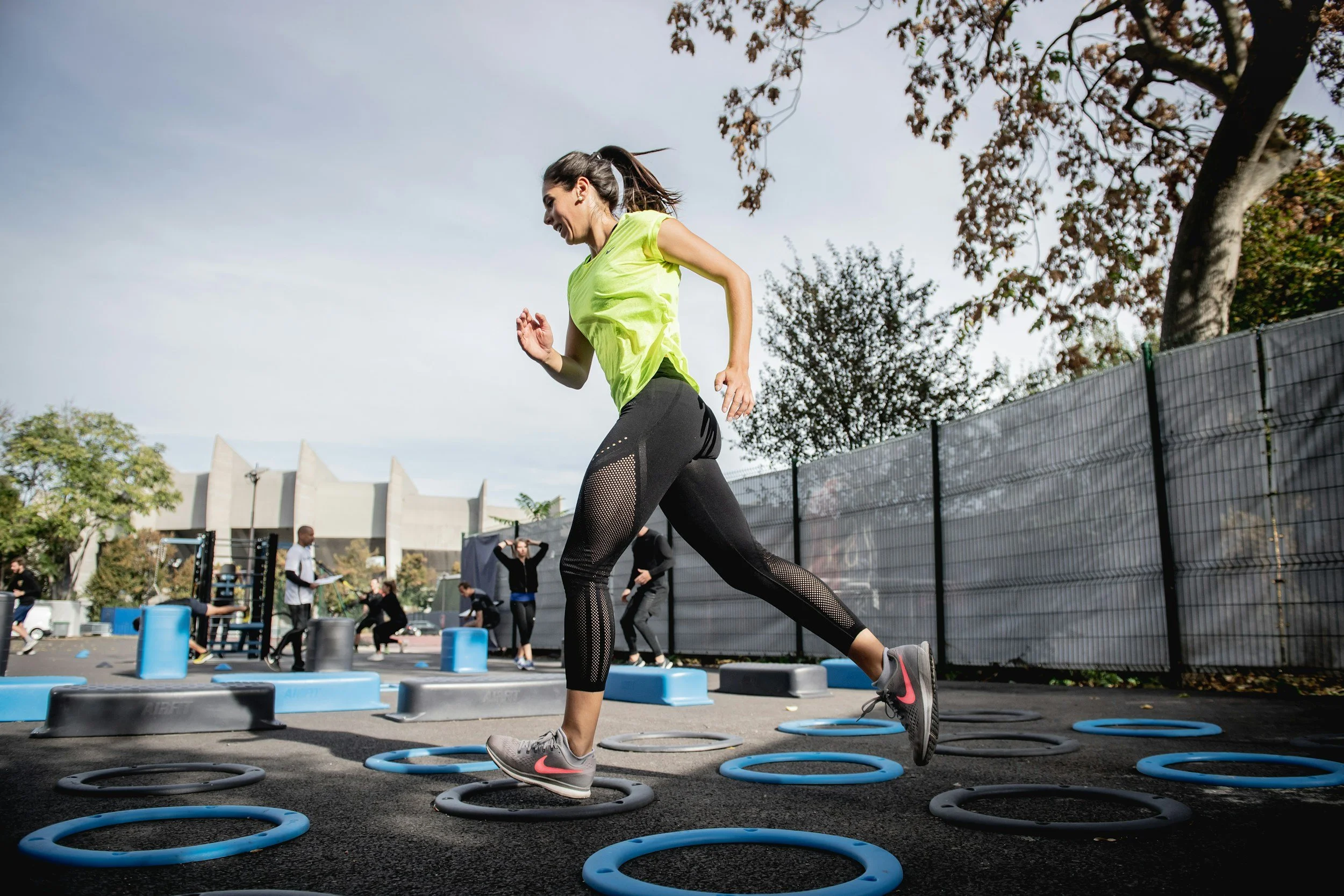 A LifeFit client performing outdoor agility drills and neuromuscular coordination patterns using floor markers during a collaborative group training session.