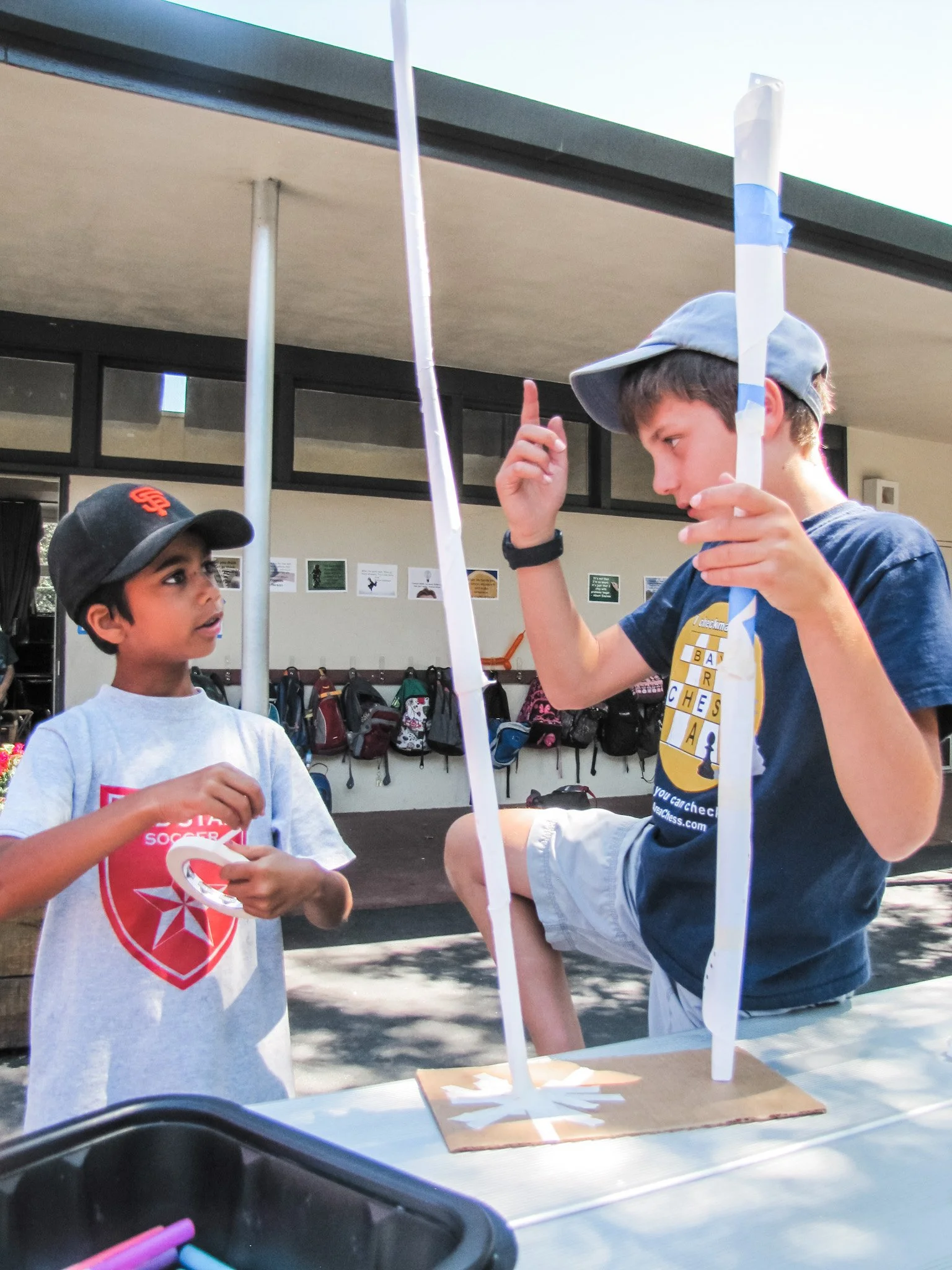 Two boys at a school science fair with a model of a wind turbine. The boy on the right is pointing at the model while the other boy looks on.