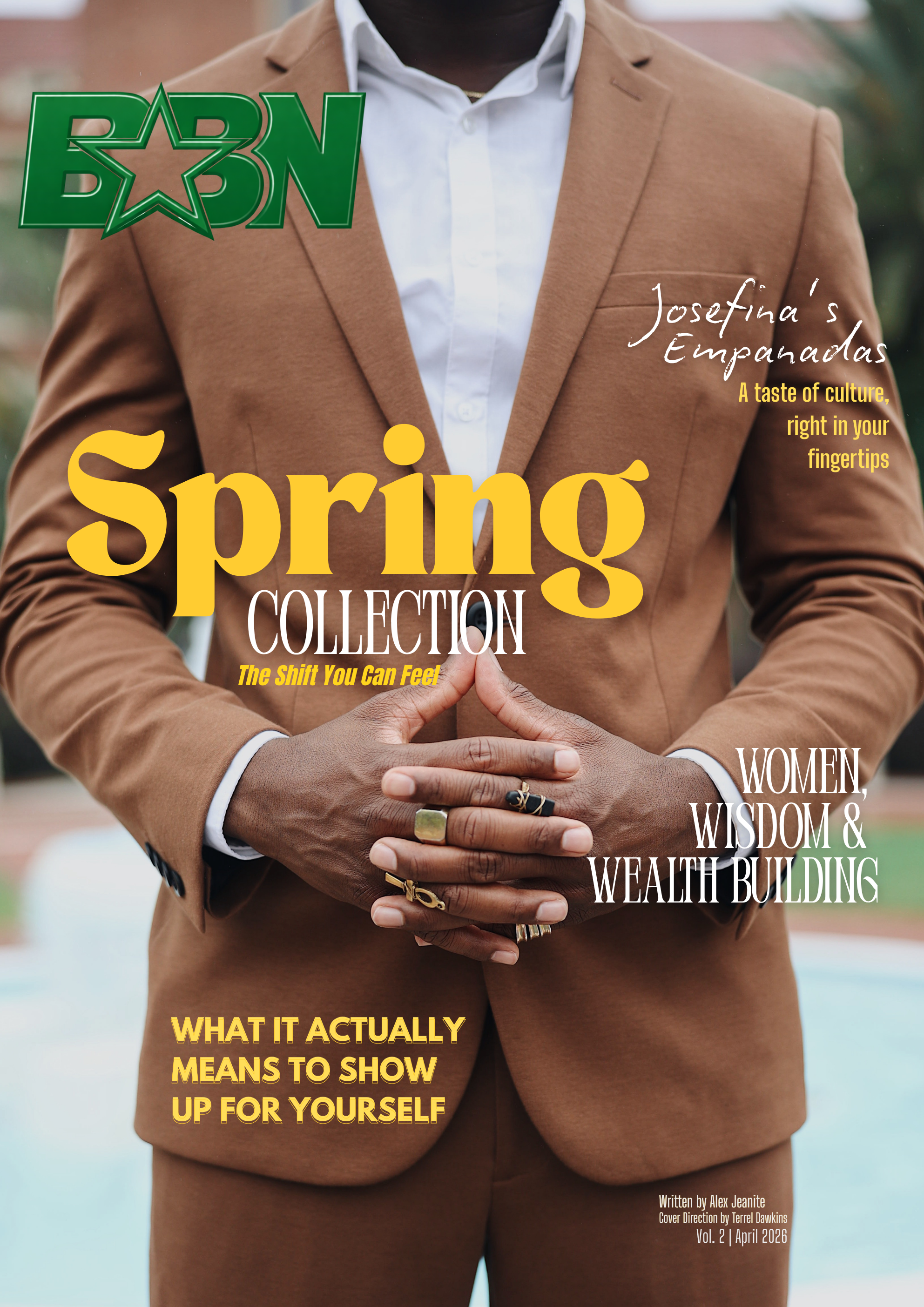 Close-up of a person wearing a brown suit and white shirt with hands held together in front, wearing rings. The magazine cover features text about women, wisdom, wealth building, culture, and self-expression.