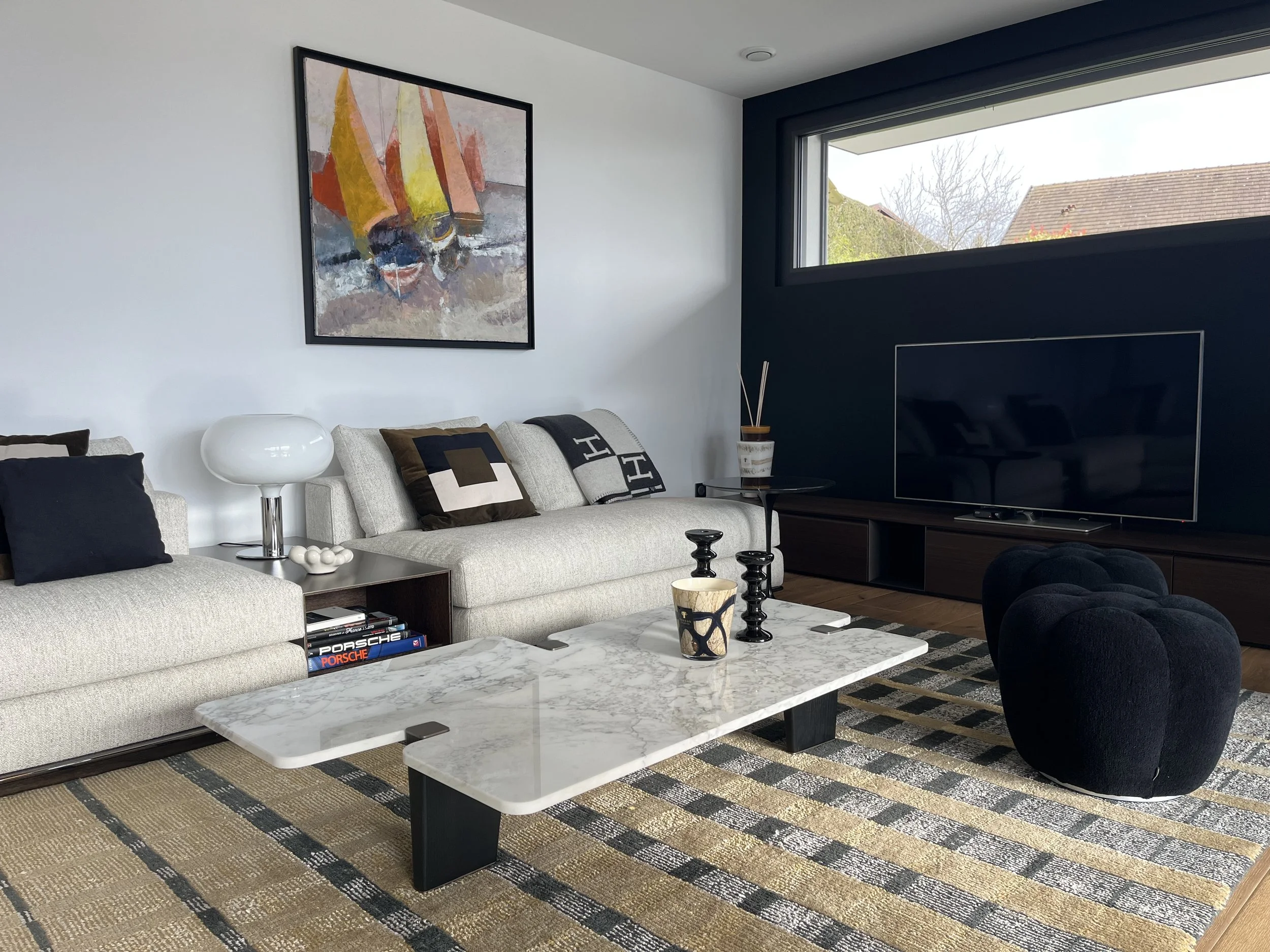 Salon contemporain avec un canapé beige, un tapis à motifs, une table basse en marbre, un tableau abstrait, une télévision, et des coussins décoratifs