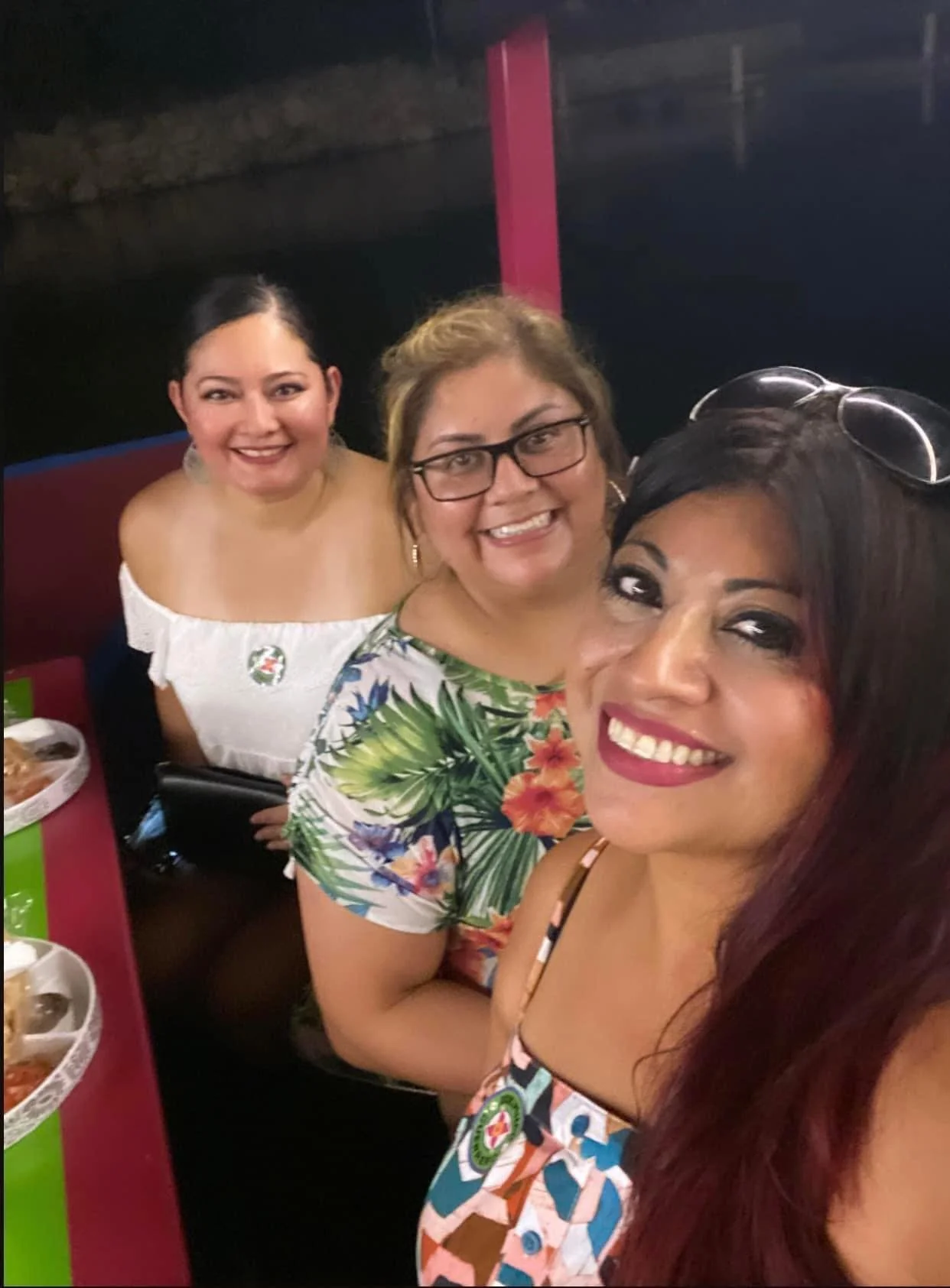 Three women smiling for a selfie at a restaurant with plates of food on the table.
