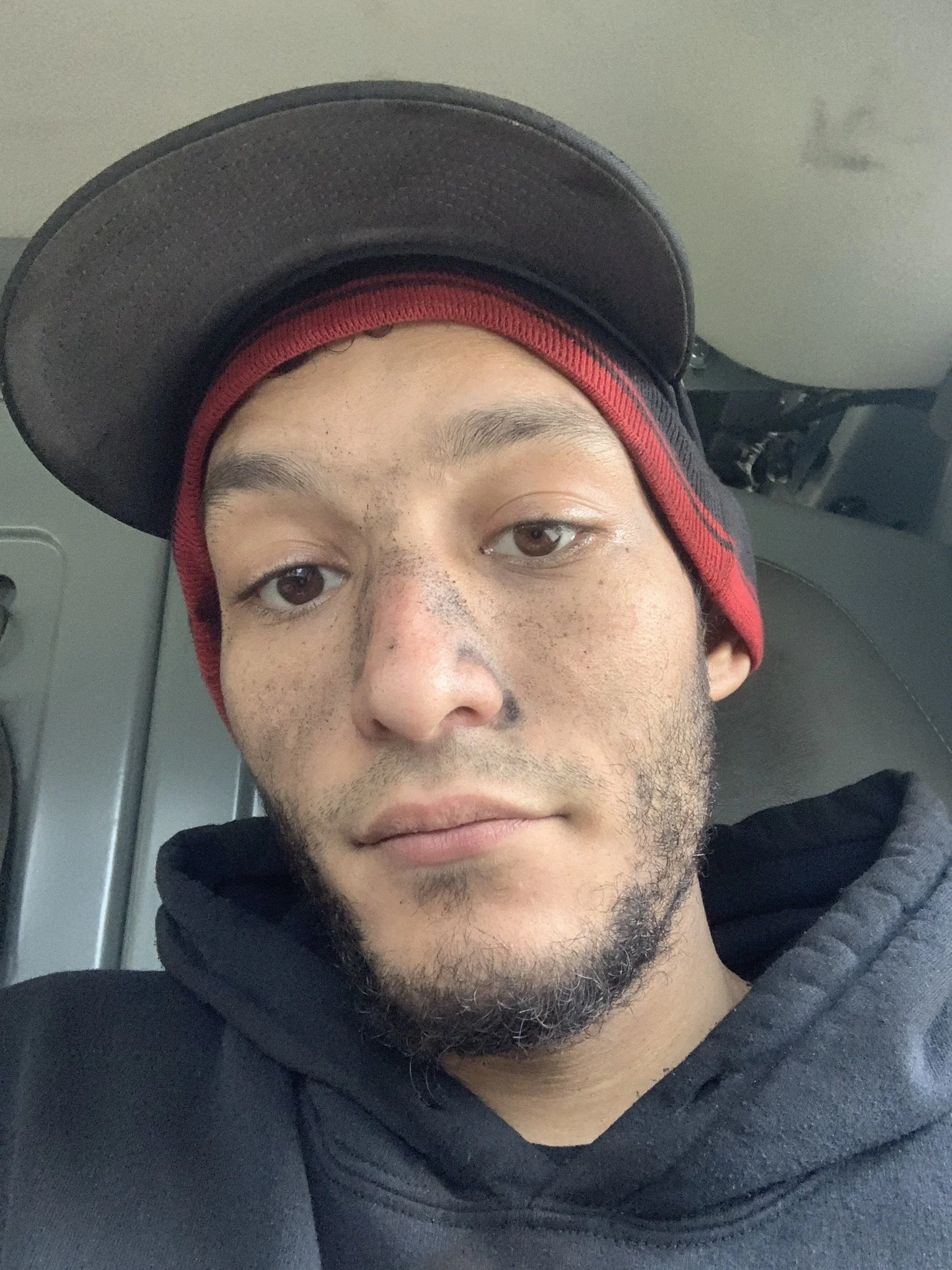 Close-up of a young man wearing a black cap, red beanie, and black hoodie.