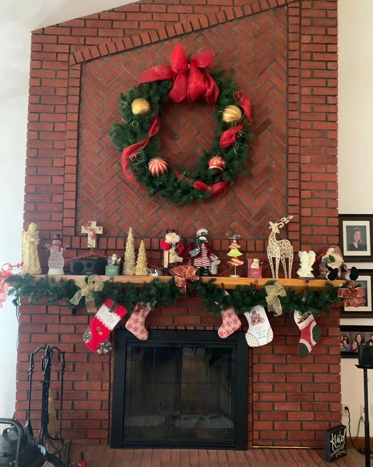 Decorated brick fireplace with green garland, red bow, and Christmas ornaments on the mantle, and Christmas stockings hanging below.