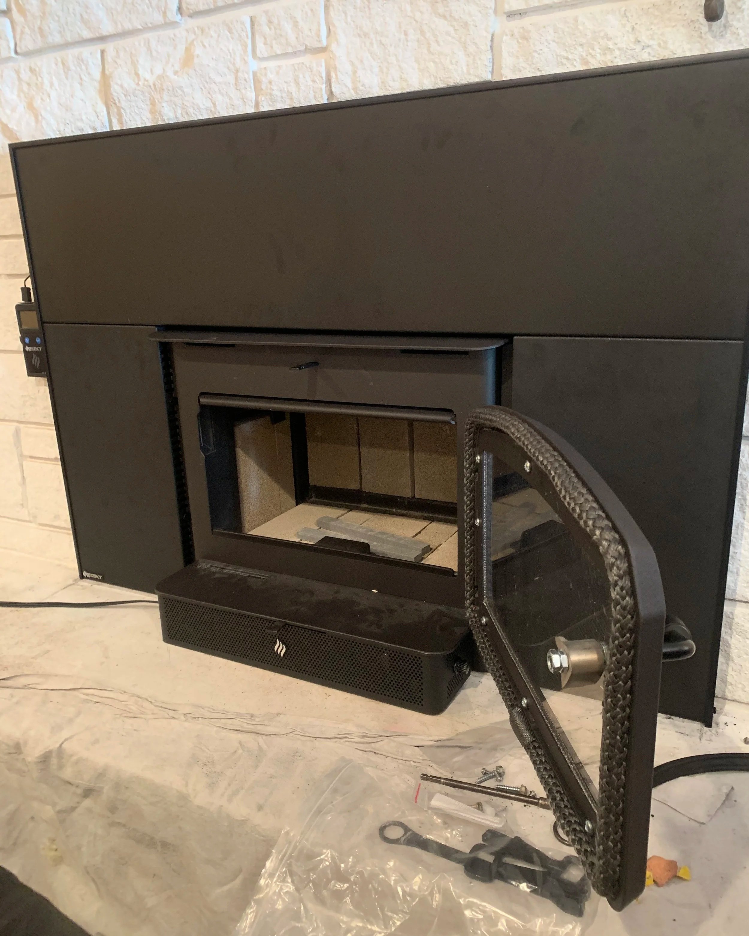 A black fireplace insert with a glass door, placed on a stone hearth. Fireplace tools and minor hardware are nearby, indicating installation or repair work.