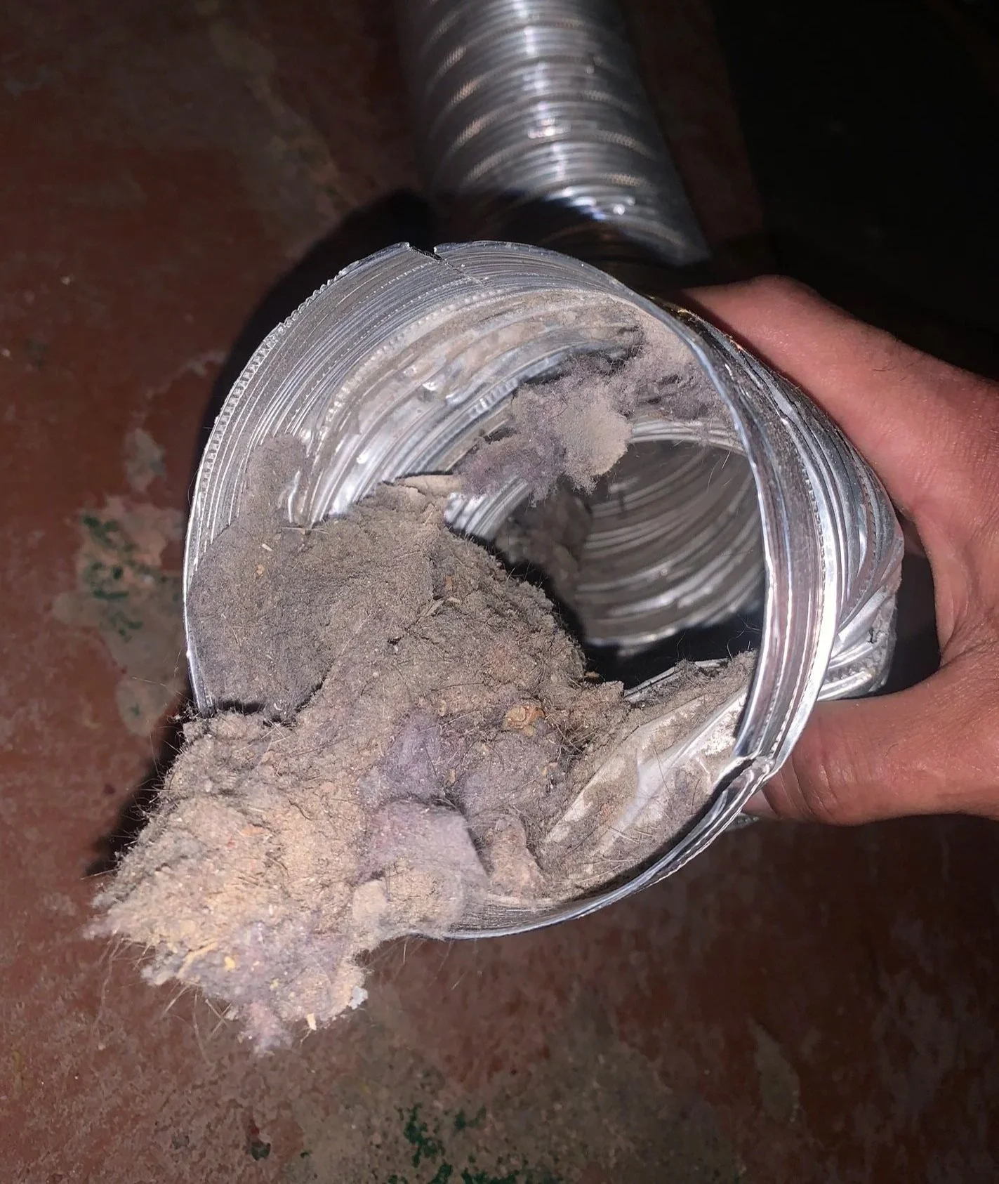 A person holding a flexible metal dryer vent duct with dirt, mud, and debris.