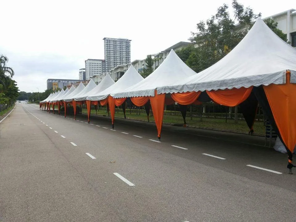 A line of white tents with orange and black drapes on a city street, with buildings and trees in the background.