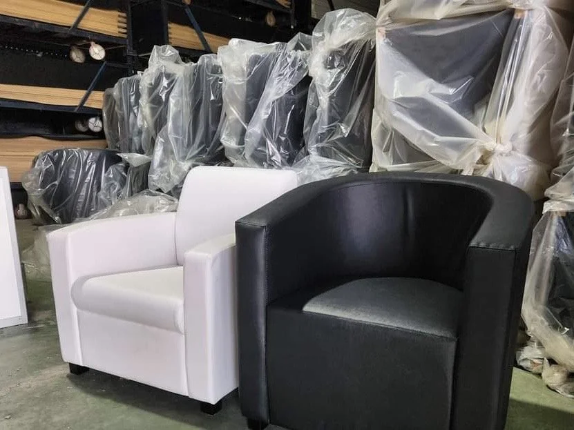 Two modern armchairs, one white and one black, placed side by side on a concrete floor, with plastic-covered furniture in the background.