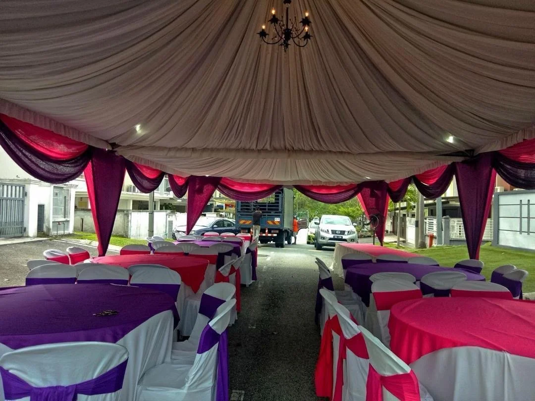 Party tent setup with tables and chairs decorated in purple, pink, and white, with a chandelier hanging from the ceiling, outdoors on a street.