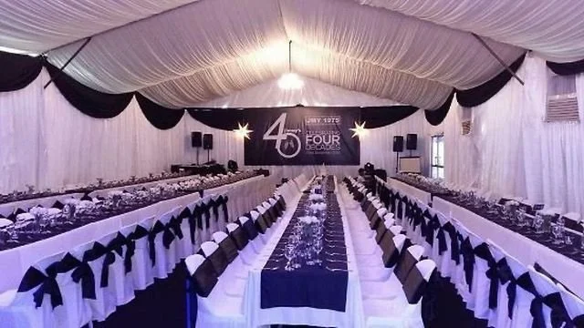 Banquet hall decorated for a 45th anniversary celebration with long tables, white linens, black bows, and a large banner reading 45 and 4th anniversary in the background.