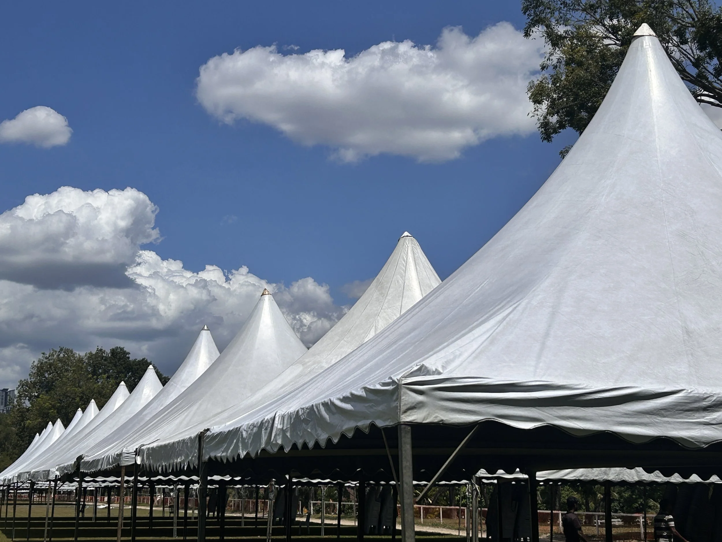A row of white tents with pointed tops set up outdoors under a partly cloudy sky.
