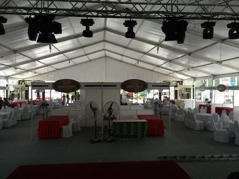 Inside a large event tent, decorated with tables covered in white cloths and red accents, set up for a celebration or banquet.