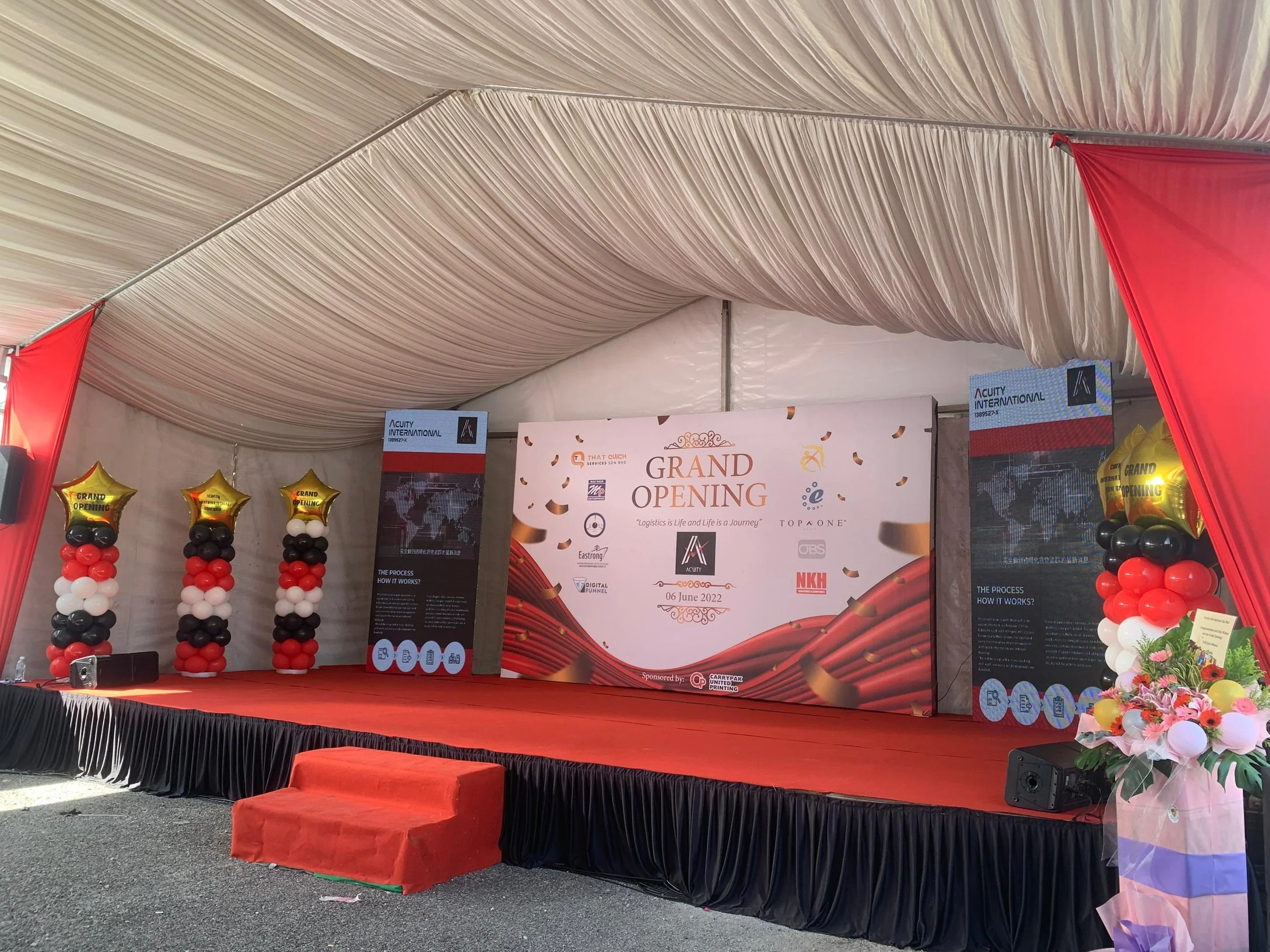 Event stage with a sign that reads 'Grand Opening' with balloons and a floral arrangement.