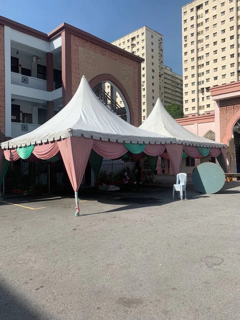A large white event tent with pink and green drapes, set up in an outdoor area with tall residential buildings in the background.