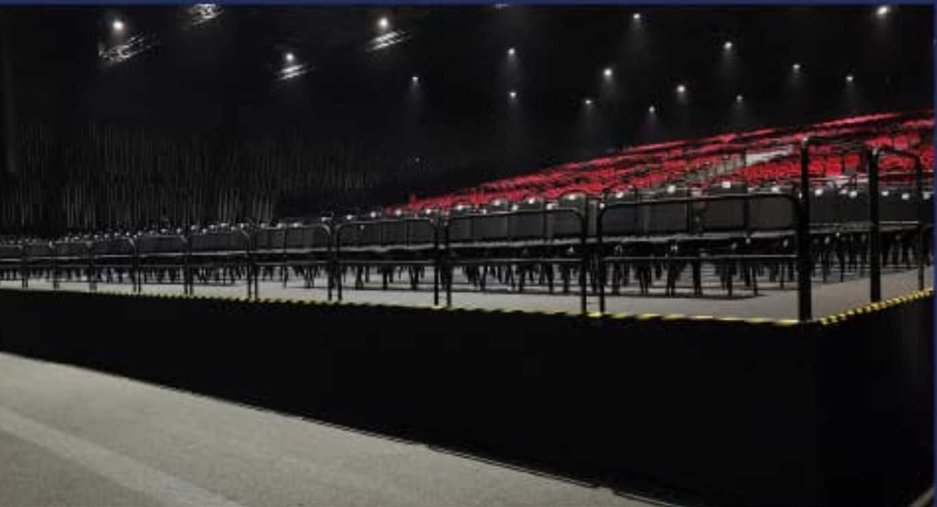 Empty auditorium with rows of black seats, black barriers, and red and black tiered seating in the background.