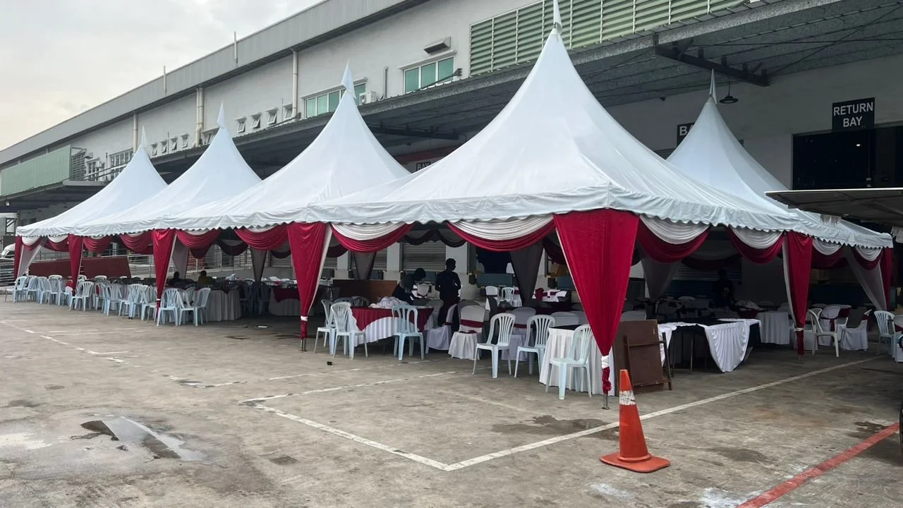 A large white event tent with red drapes and multiple tables with white chairs set up underneath, likely for a celebration or gathering outside a building.
