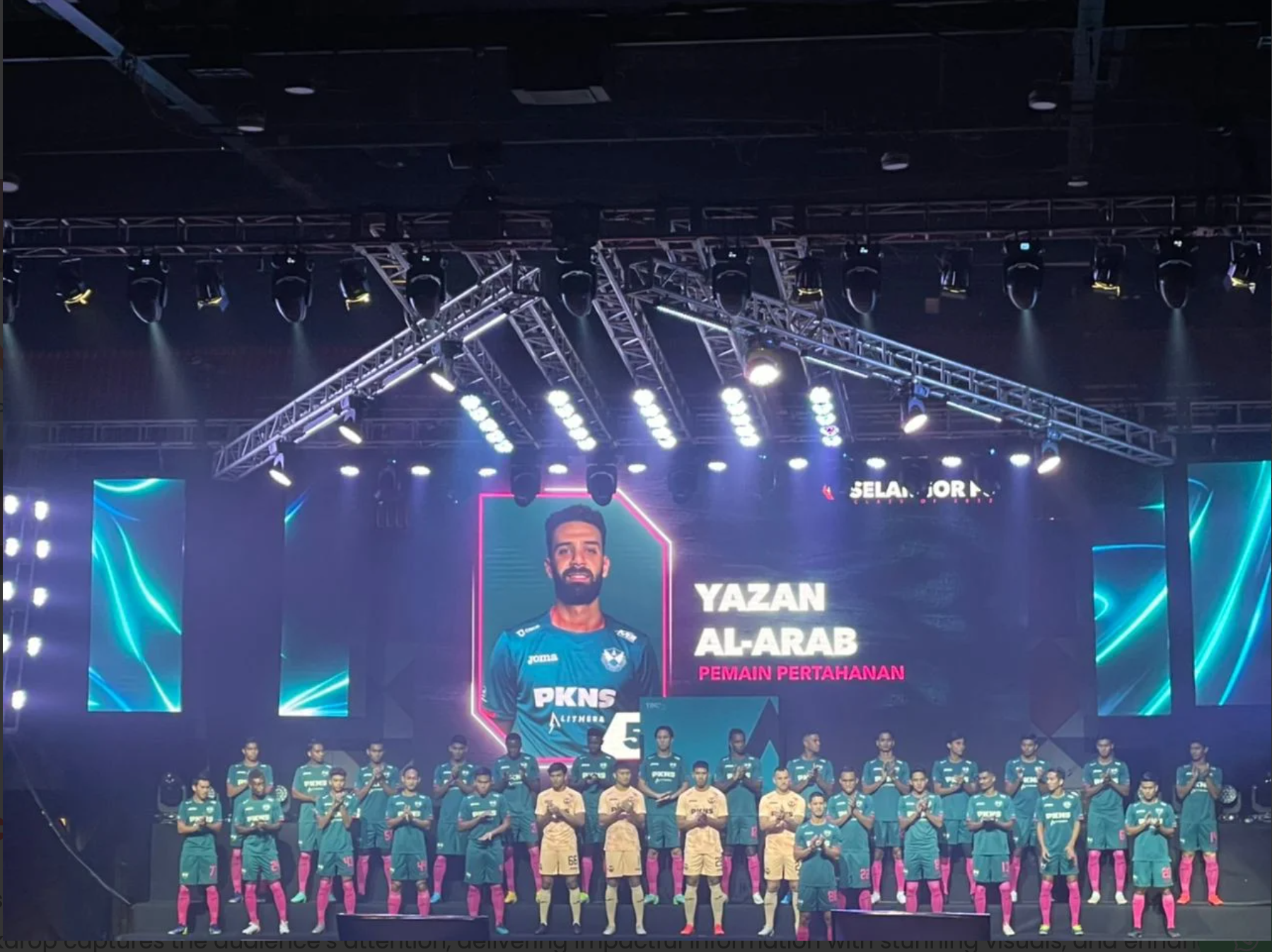 A group of soccer players in uniforms standing on a stage during a presentation, with a large screen overhead displaying the name Yazan Al-Arab and the title Peman Pertahanan. The stage is illuminated with bright lights and there are large digital sc