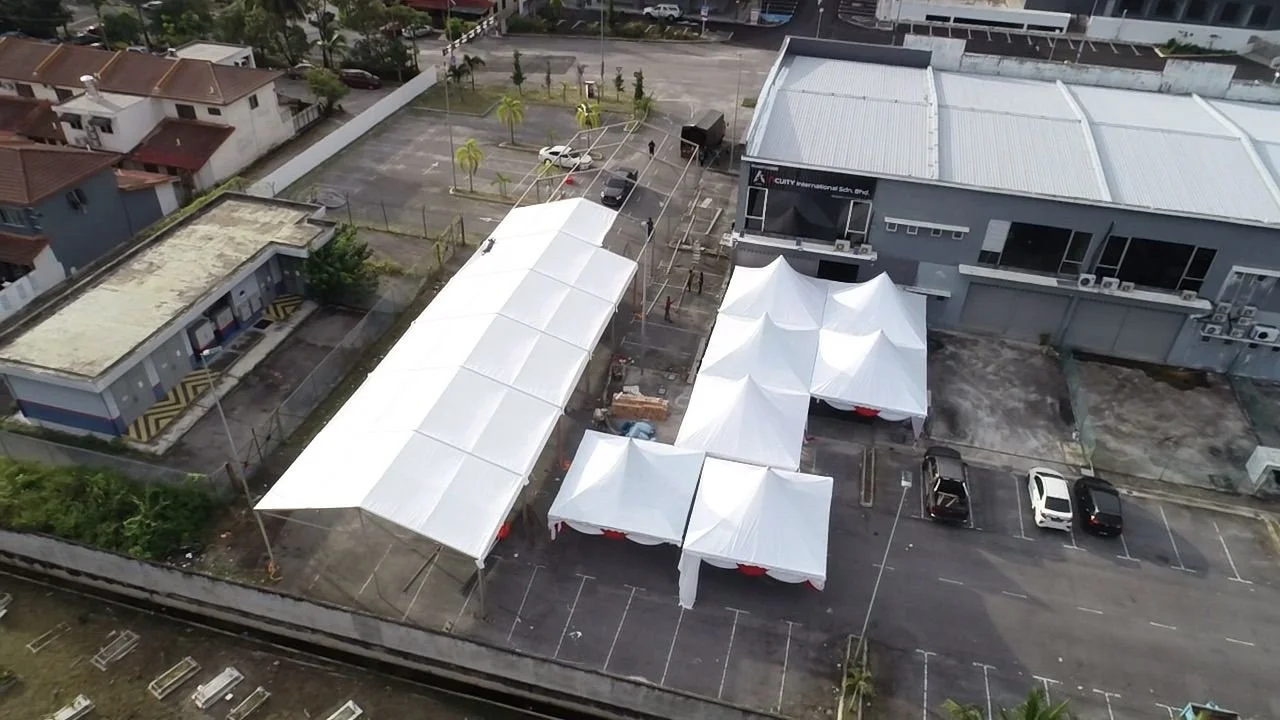 An aerial view of a parking lot with covered tents arranged for an event outside a large commercial building.