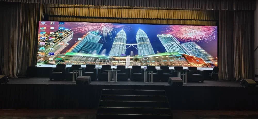 Stage with a large LED screen displaying a cityscape with fireworks, and several chairs and tables set up in front.