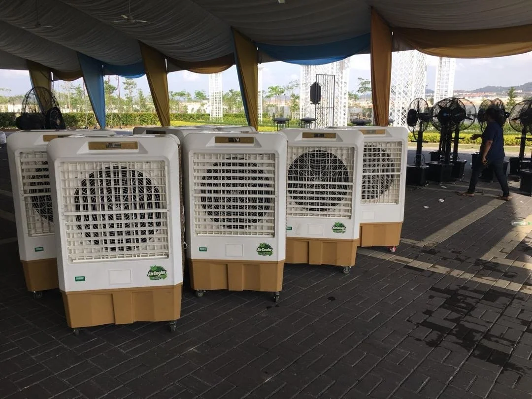 A row of portable air coolers on a dark brick floor under a canopy, with fans in the background and a person walking past.