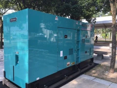 Blue industrial generator outside near a tree and a bench in a park-like setting.