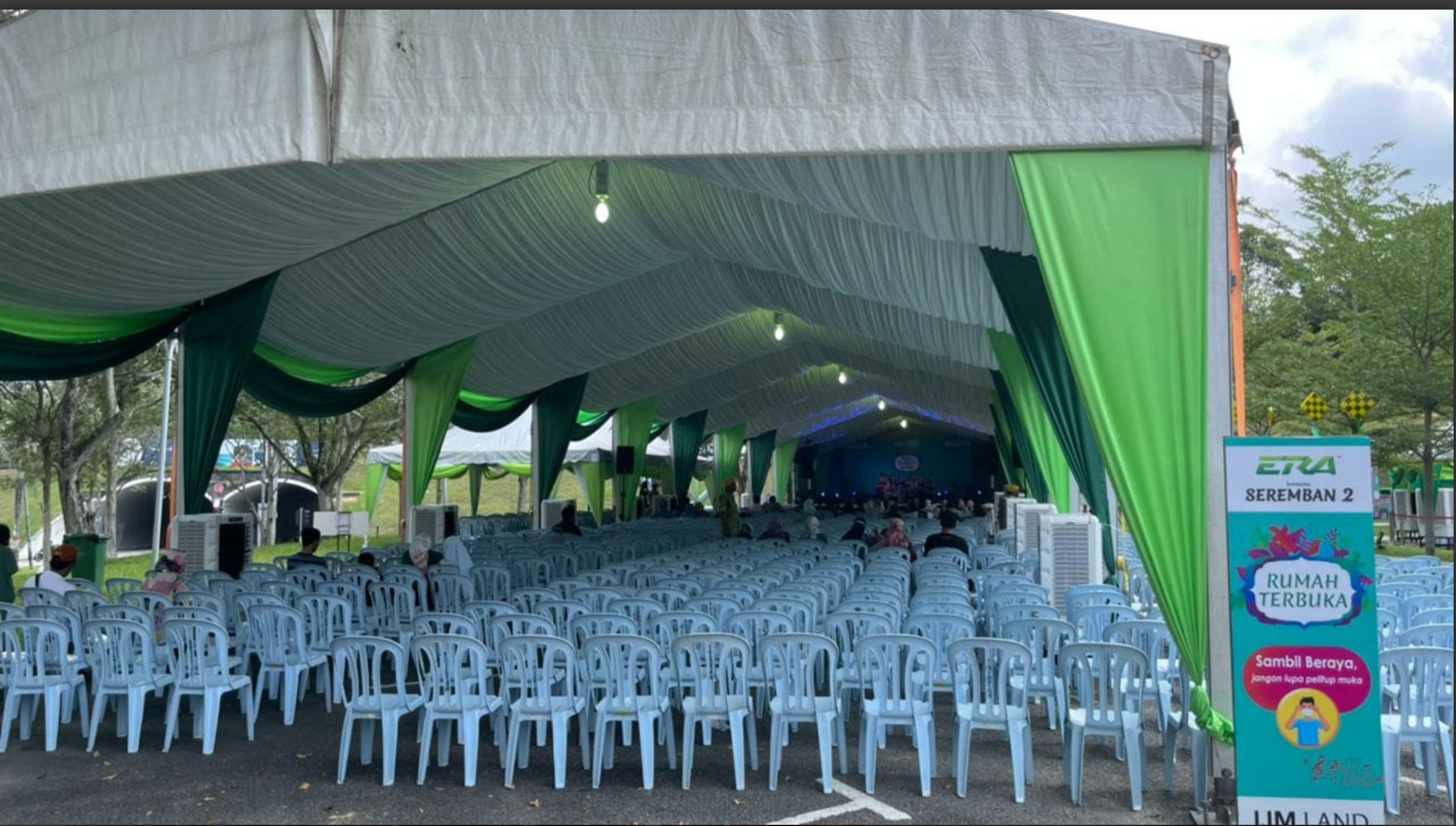 Outdoor event tent with seating and a stage, with trees in the background and a sign indicating a community or health event.