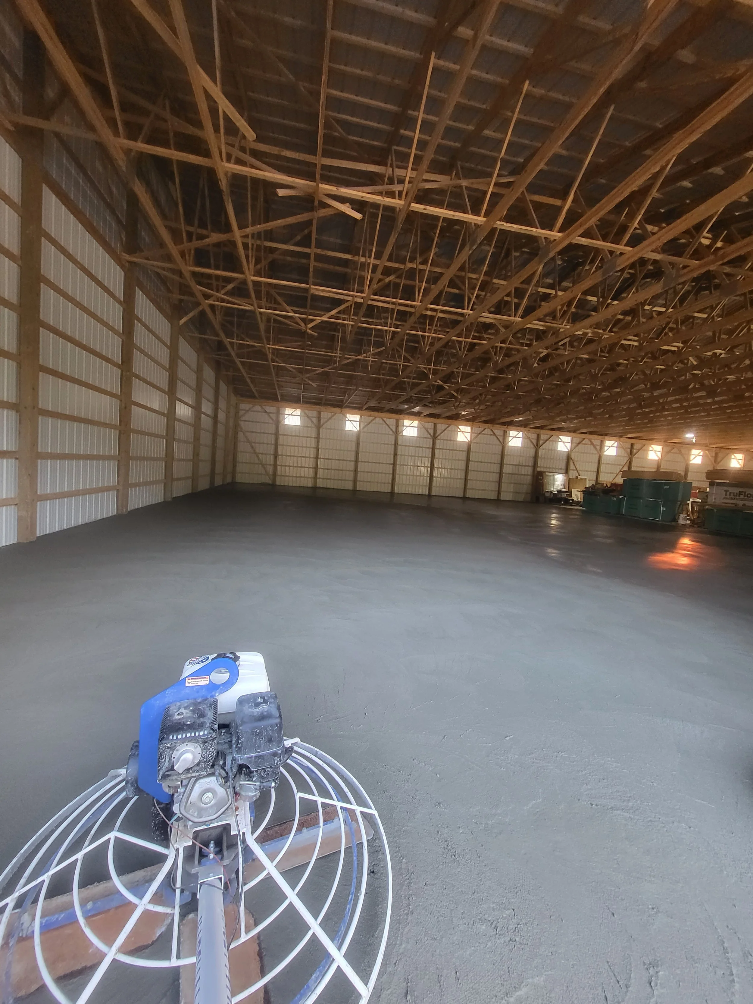Interior of a large barn under construction with freshly poured concrete flooring and a concrete power trowel in the foreground.