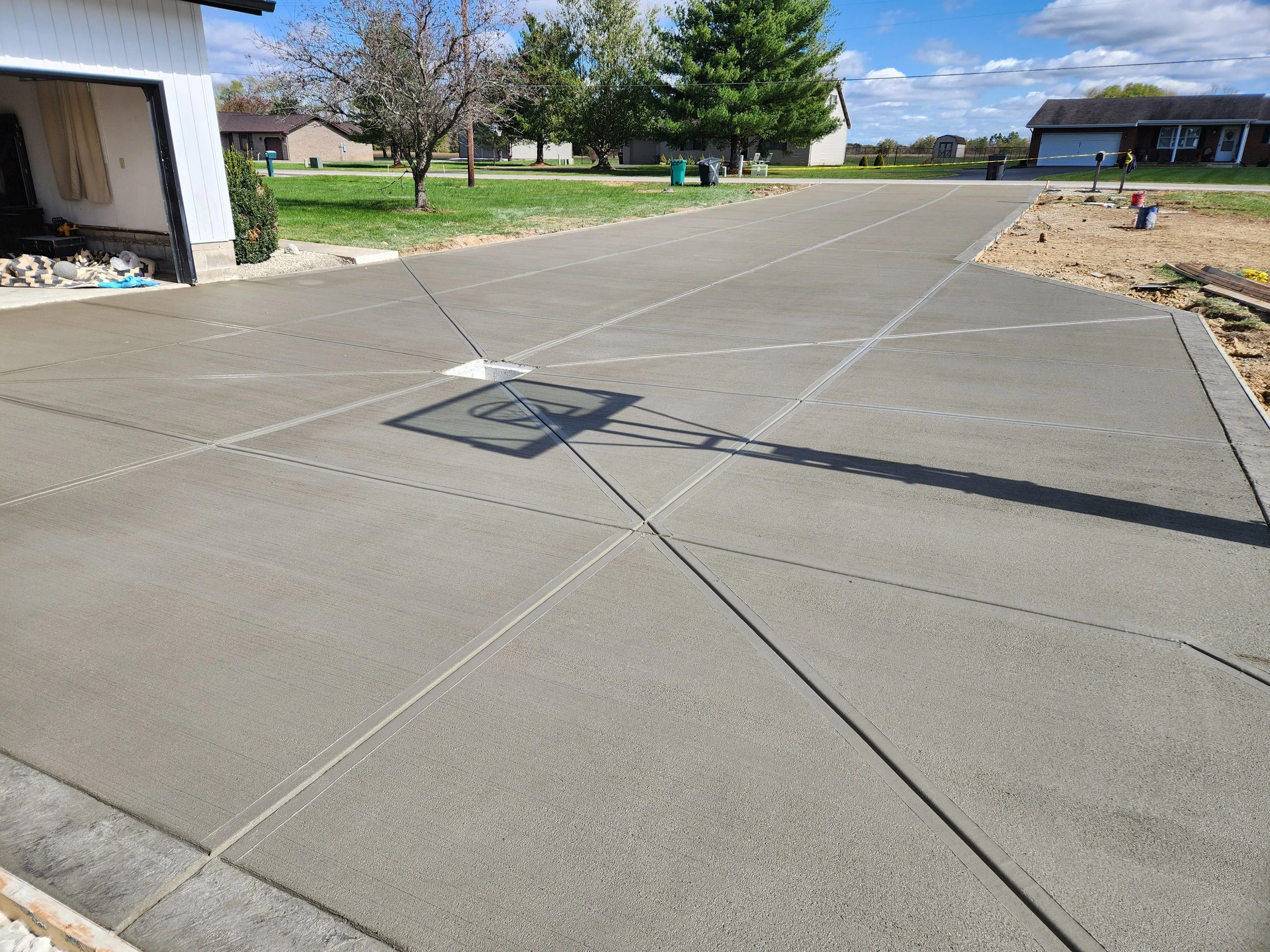 Freshly poured concrete driveway with wooden formwork, adjacent to a garage and yard, in a suburban neighborhood.