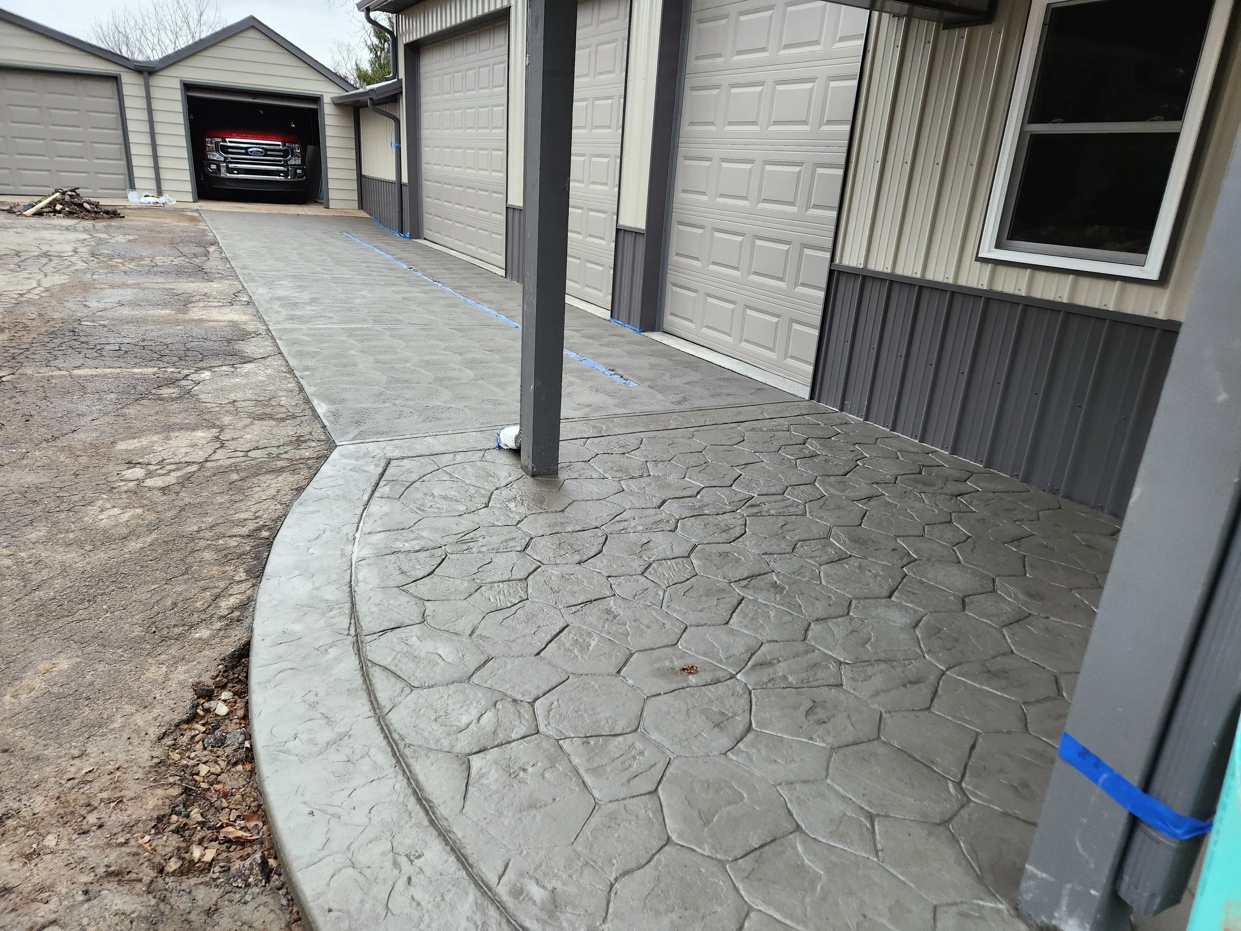 Newly paved concrete sidewalk and driveway in front of garages with a parked truck inside one of the garages.