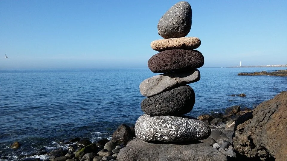Stack of seven stones balanced on a rocky shoreline with ocean and blue sky in the background.