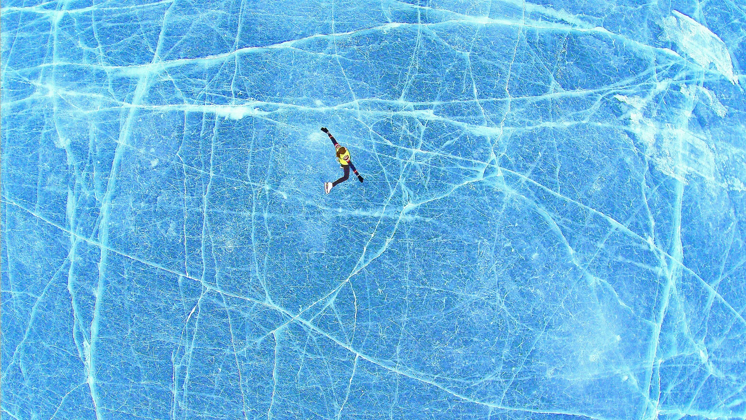 Freestyle female skater skating on a blue azure frozen lake