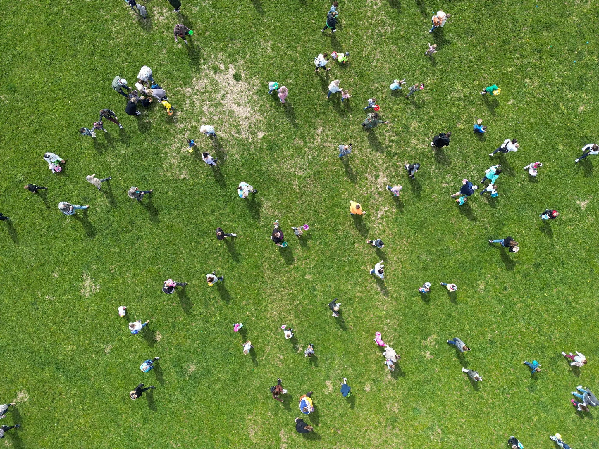 Aerial view of a group of people walking on a grassy field, some carrying bags or backpacks.