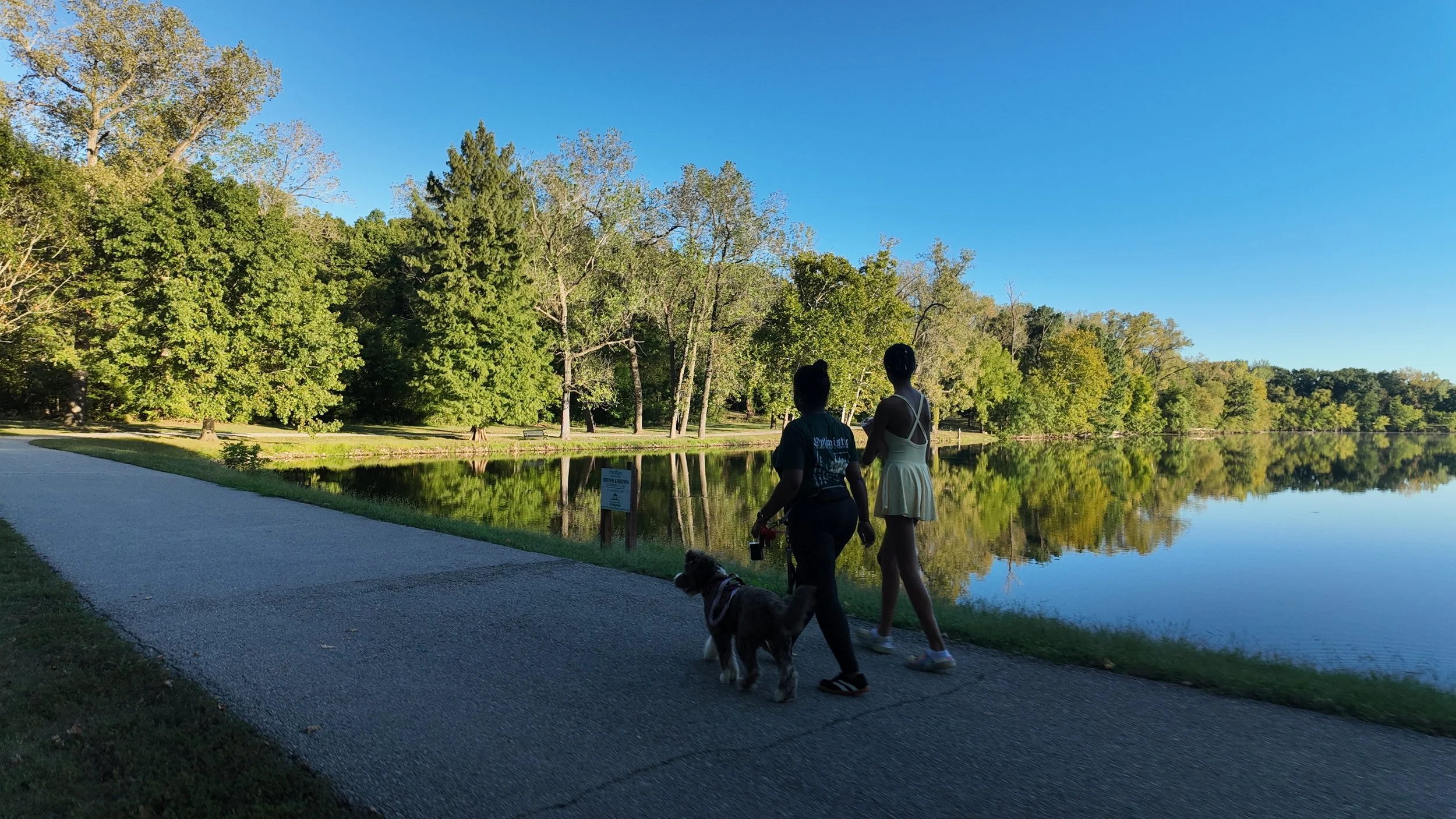 Image of two people walking their dog in front of a lake
