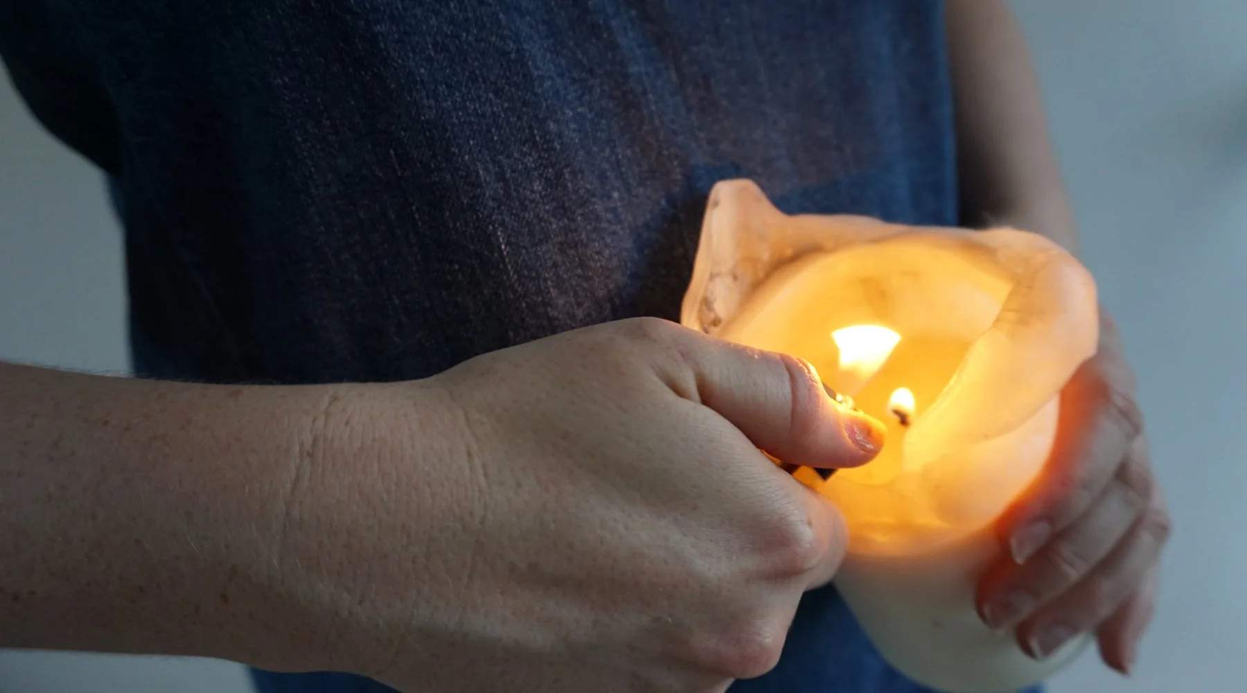 Person holding a lit candle in a hollowed-out shell or bowl