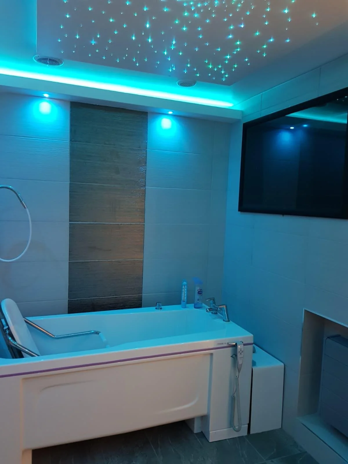 A modern bathroom with a bathtub, TV on the wall, and starry sky ceiling lights.