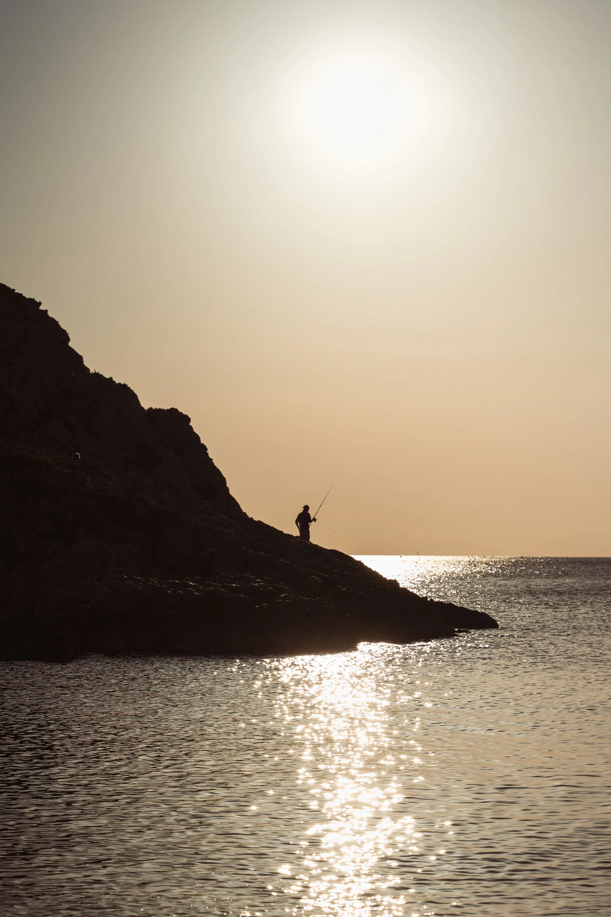 Silhouette d'un pêcheur debout sur une falaise au bord de la mer au coucher du soleil en région PACA