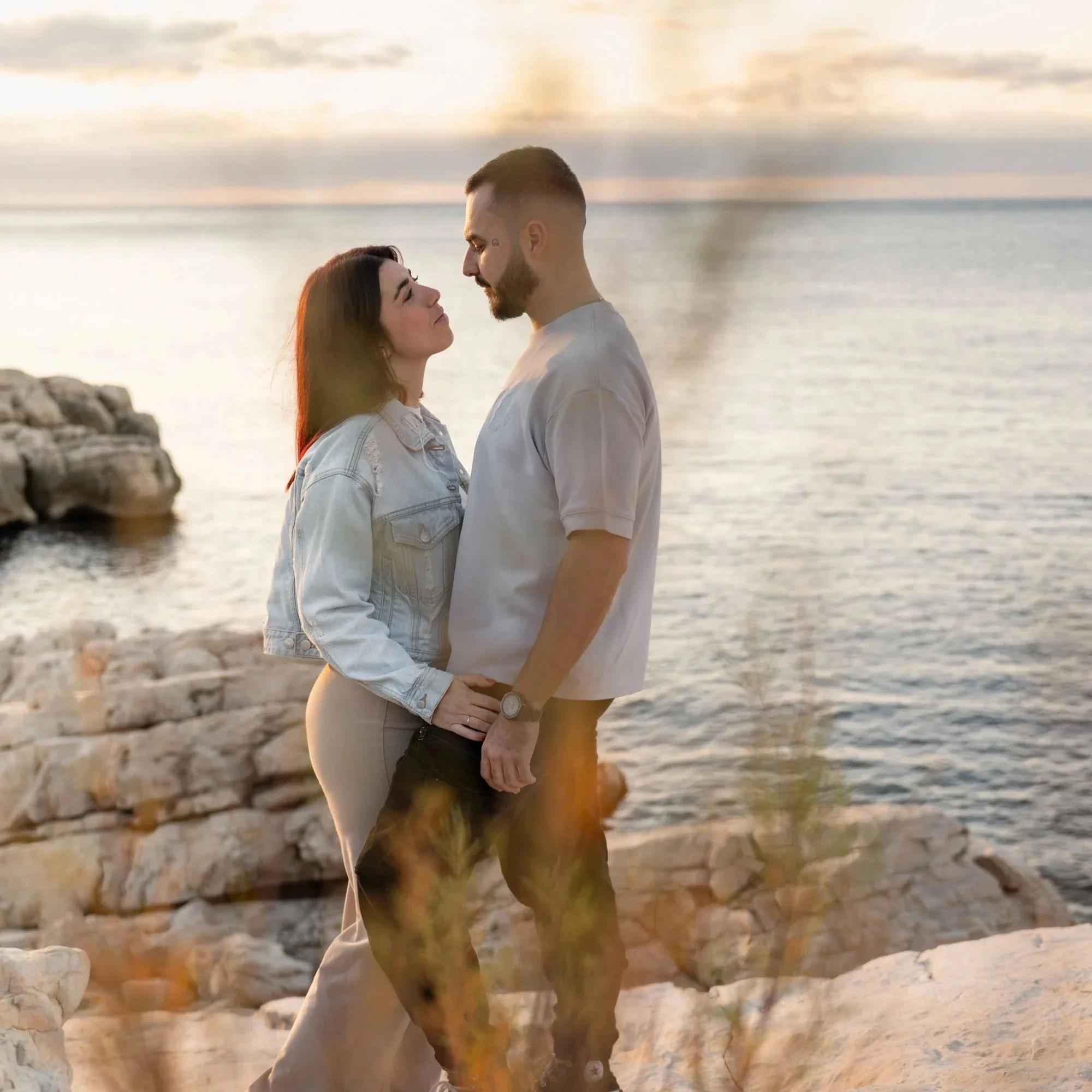 Un couple marchant côte à côte près de la mer au coucher du soleil, se regardant tendrement.