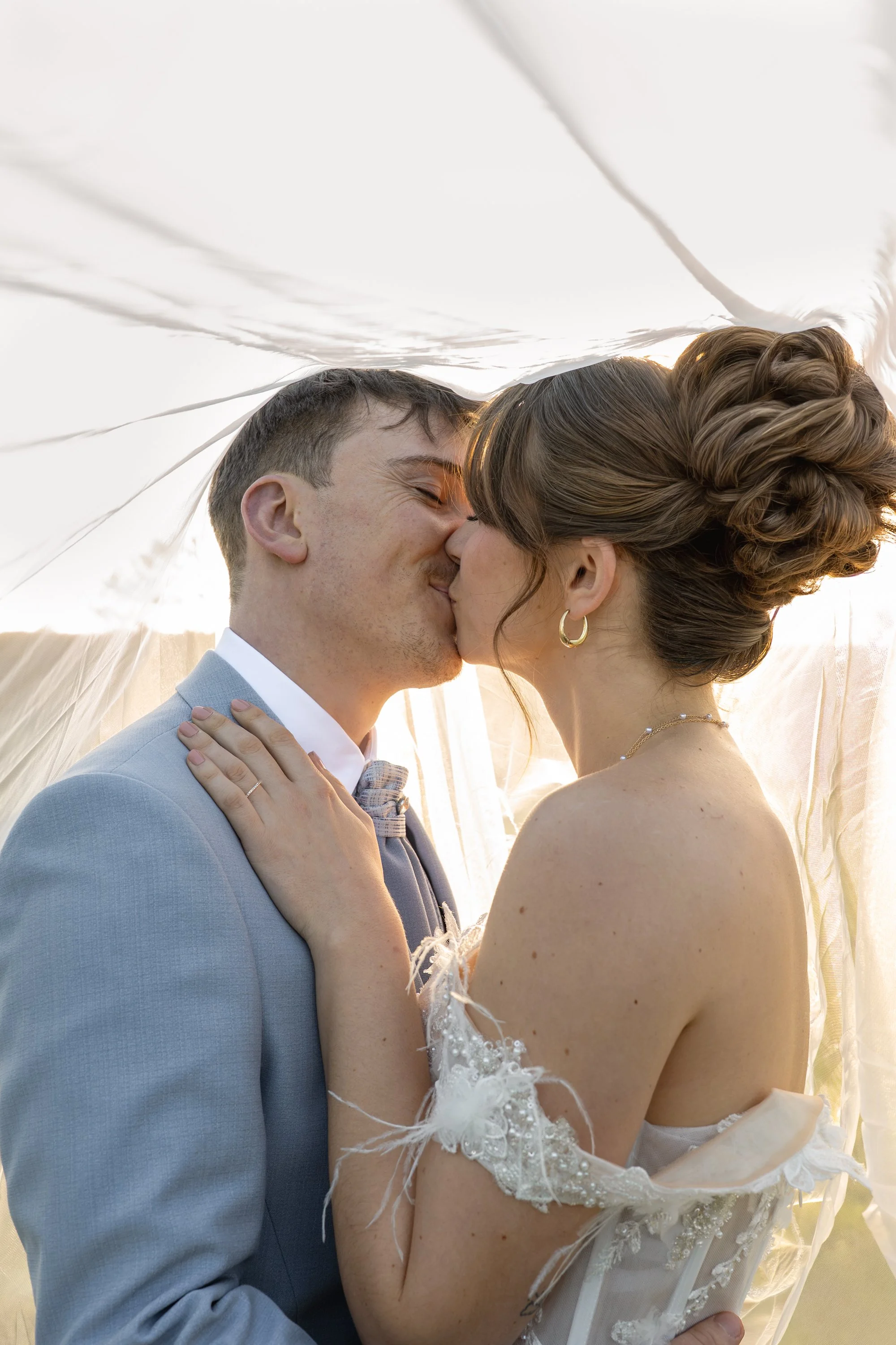 Un couple de jeunes mariés s'embrassent sous un drap blanc pendant leur mariage