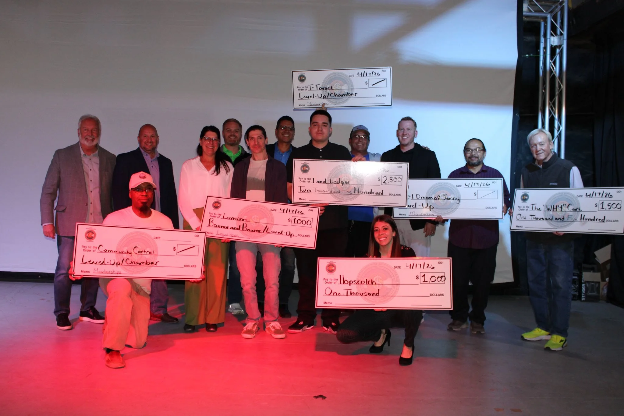 A group of people on stage holding oversized checks for different amounts, celebrating an event or achievement of Soco Entrepreneur Event. Cassime Joseph highlighted Community Central.