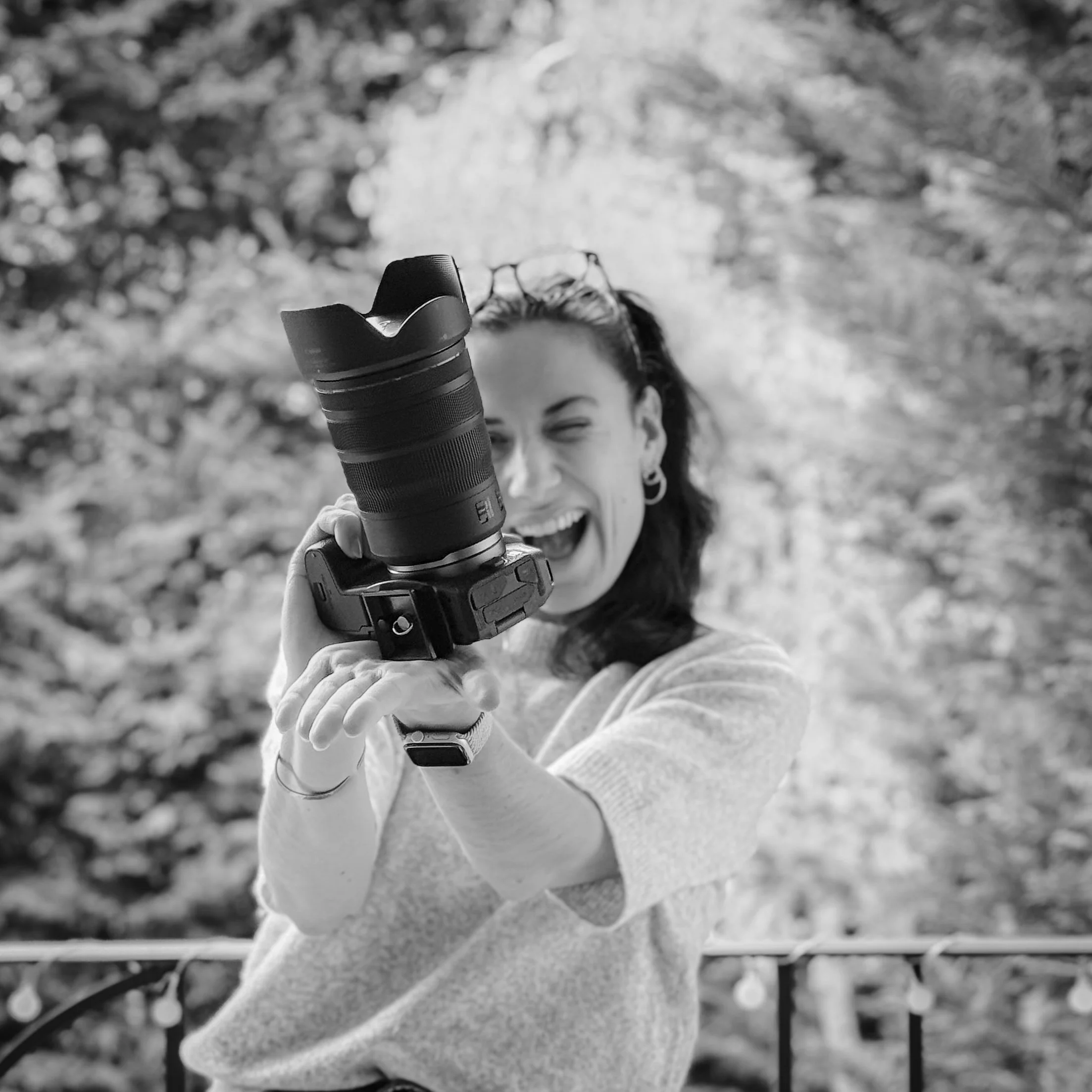Une femme souriante brandissant un appareil photo dans un cadre extérieur naturel.