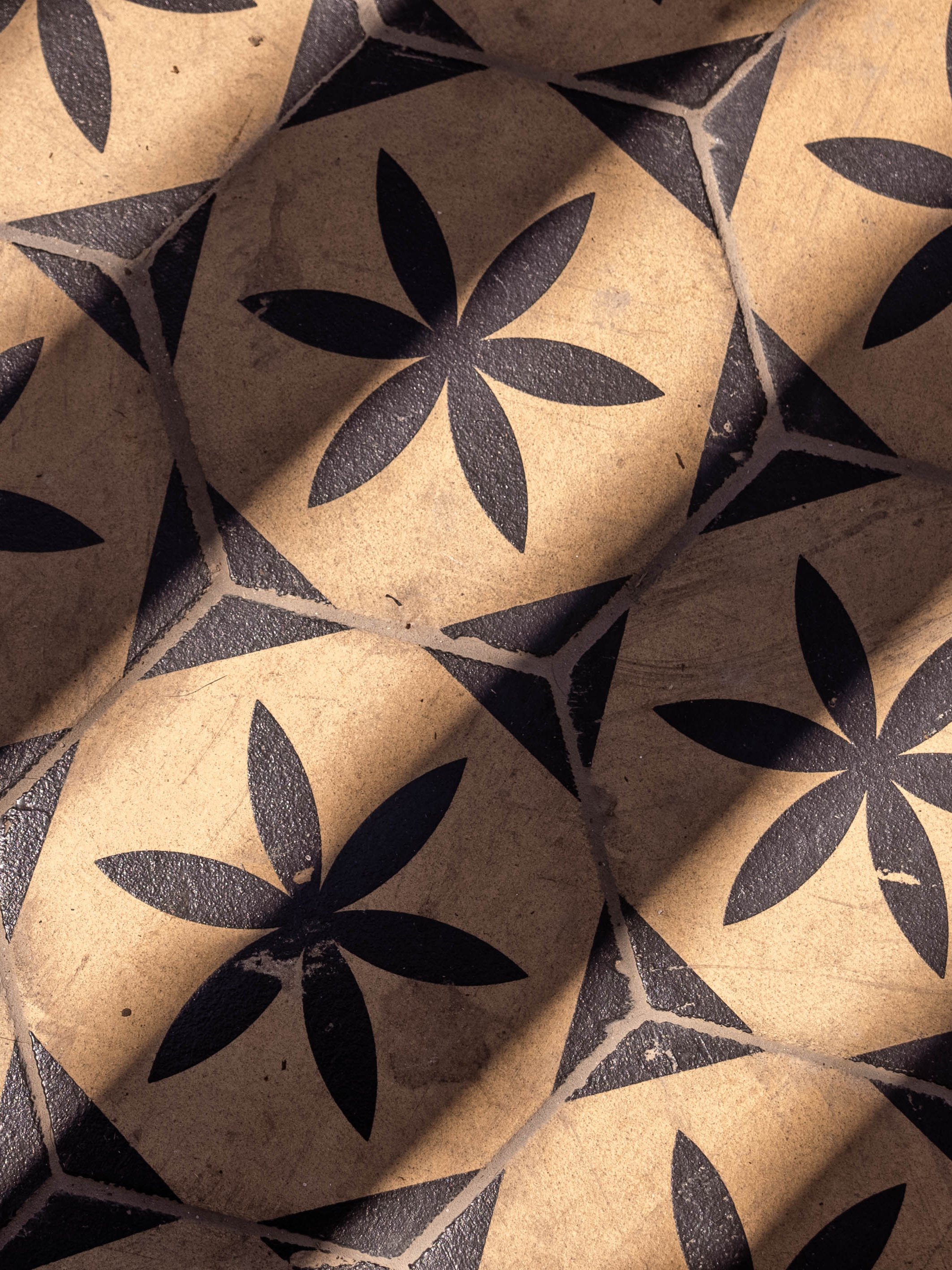 Close-up view of patterned paper or tiles with a black floral design on a tan background.