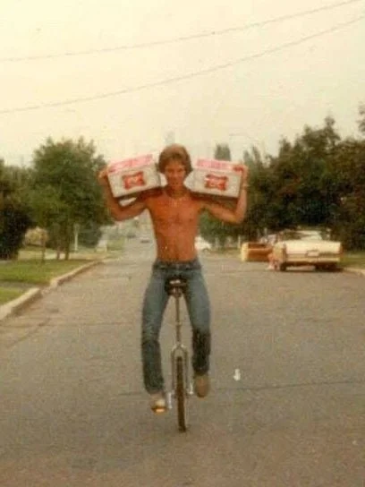 A young man riding a bicycle on the street, carrying boxes on both shoulders.