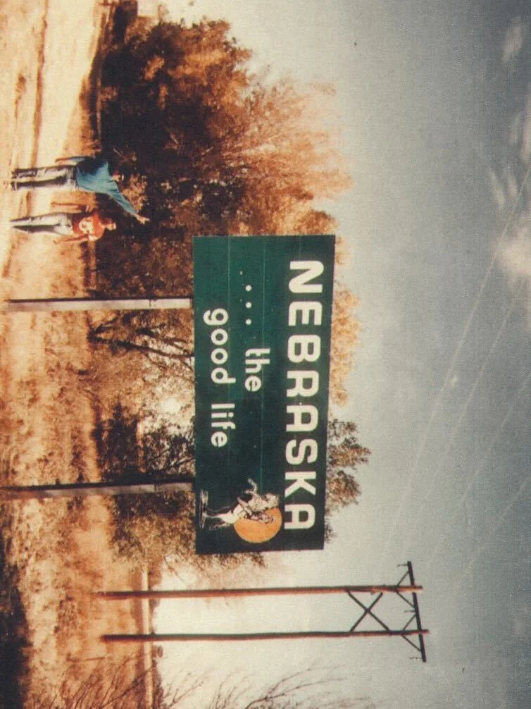A green highway sign on the side of a road that reads, "NEBRASKA the good life,