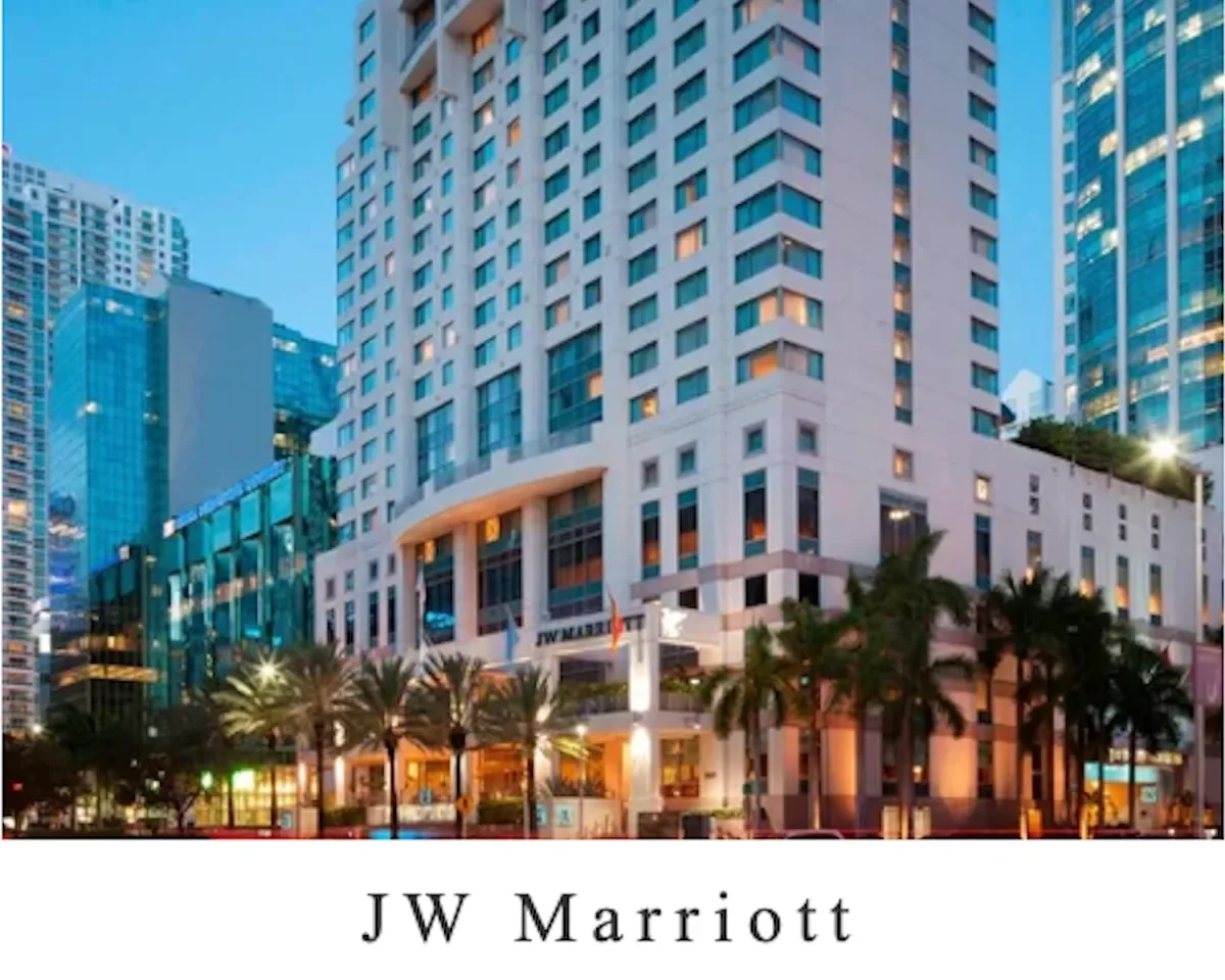 The JW Marriott hotel in a city with tall modern buildings, palm trees in front, and the hotel illuminated at dusk.