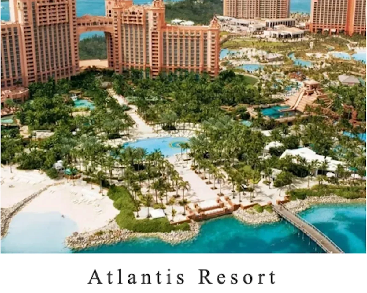 Aerial view of Atlantis Resort with pinkish high-rise buildings, multiple pools, palm trees, and a bridge over turquoise water.
