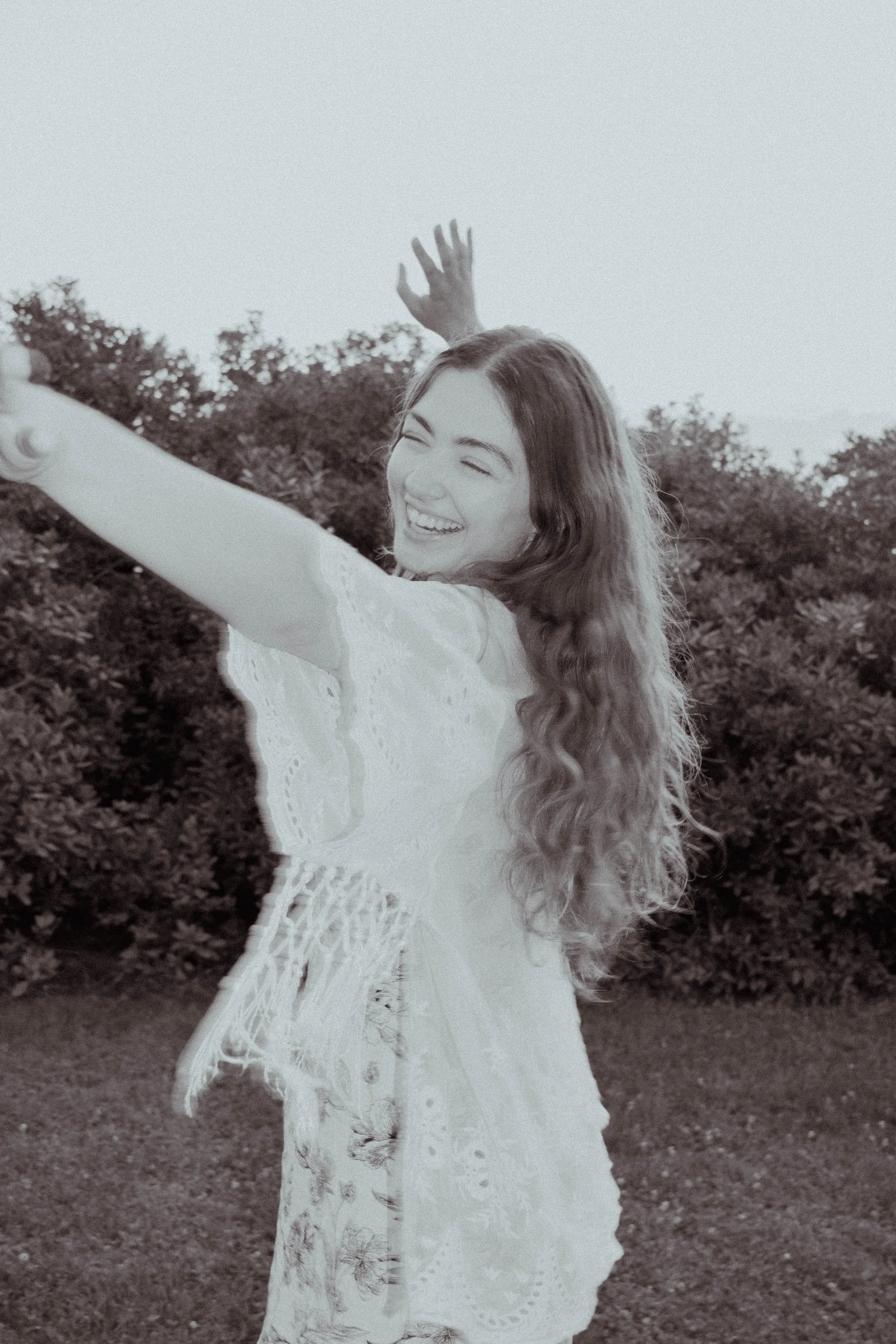 Black-and-white portrait of Julia E. Christian smiling outdoors with arms raised, capturing a light, joyful moment.