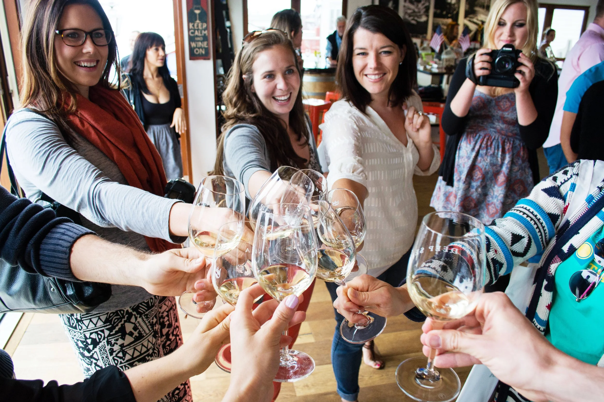 A group of people raising glasses of white wine in a toast at a celebration or gathering, smiling and enjoying each other's company indoors.